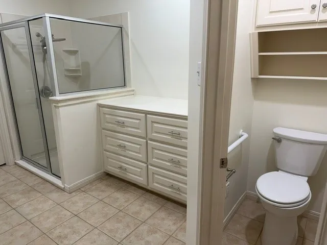 Glass-enclosed shower with a built-in shelf, adjacent storage cabinetry with multiple drawers, and tiled flooring