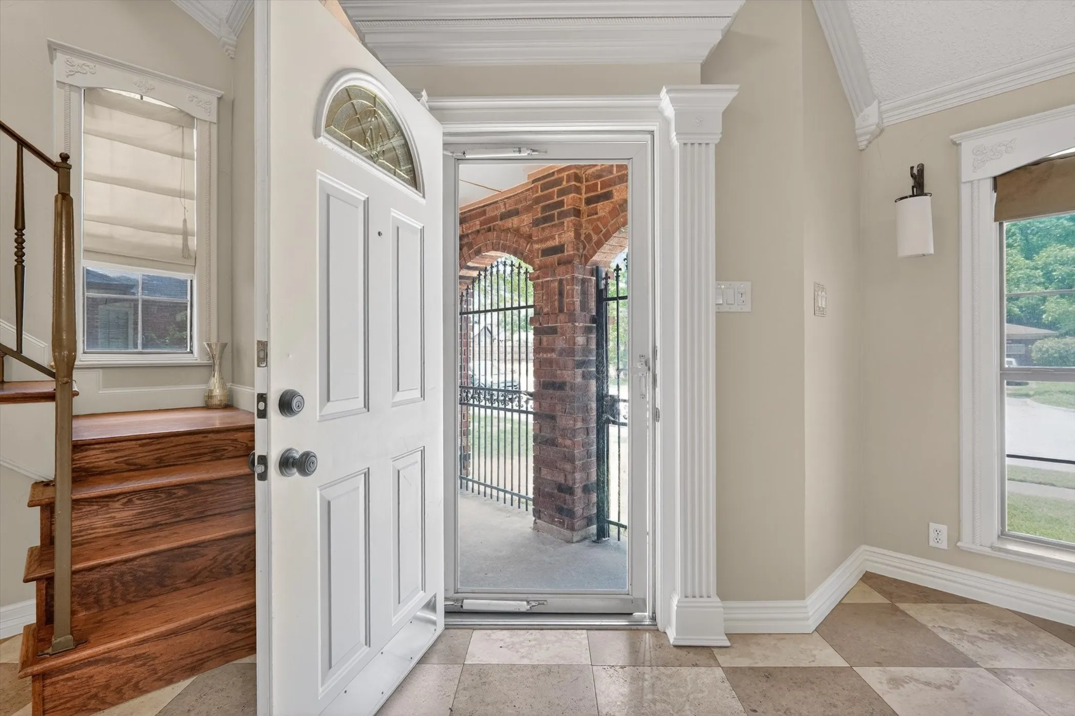 Entry foyer featuring checkerboard tile flooring, a solid wood staircase with metal railing, and a white paneled front door with an arched transom