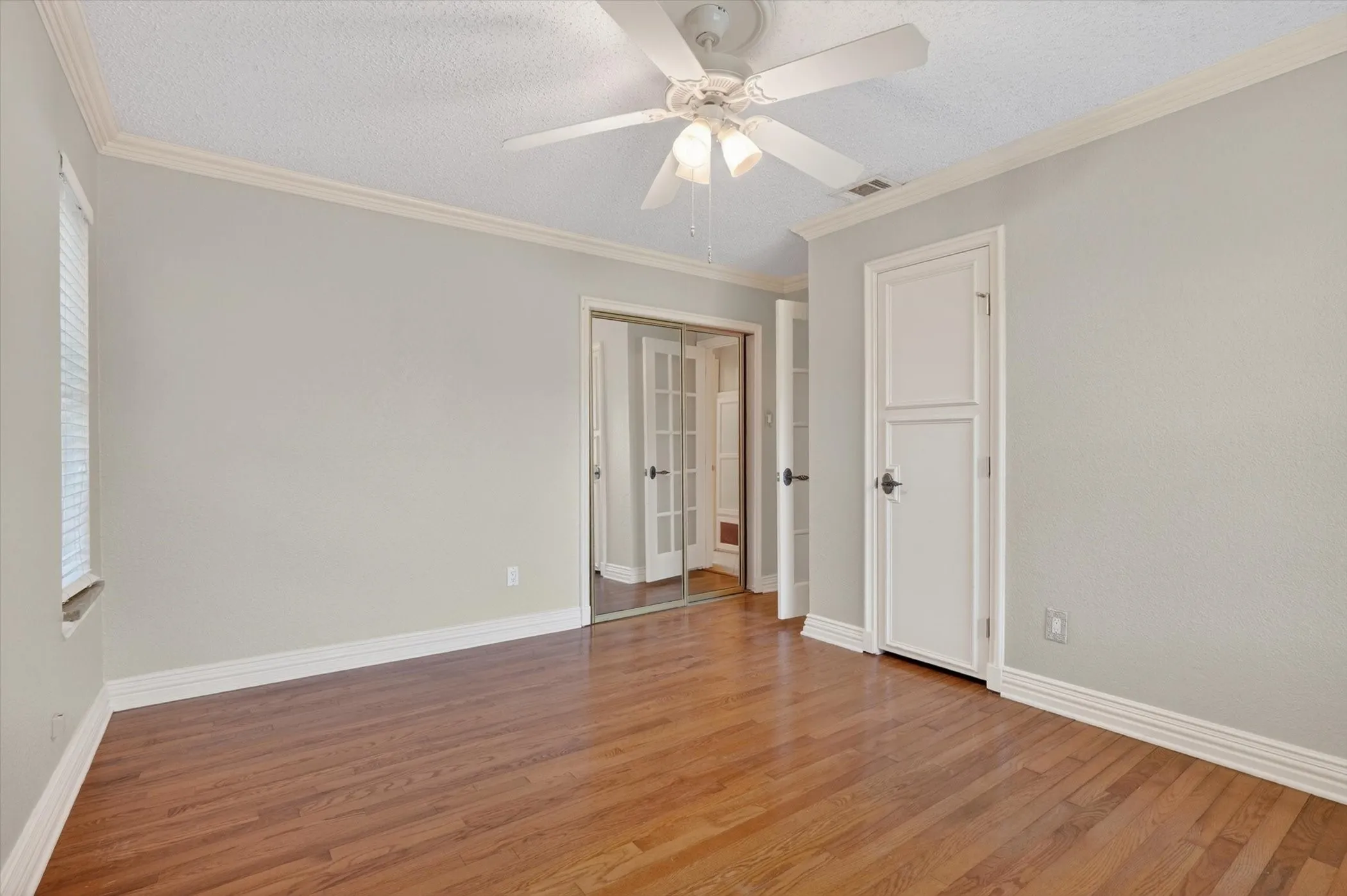 Room featuring wood-finish flooring, a ceiling fan with integrated lighting, and crown molding