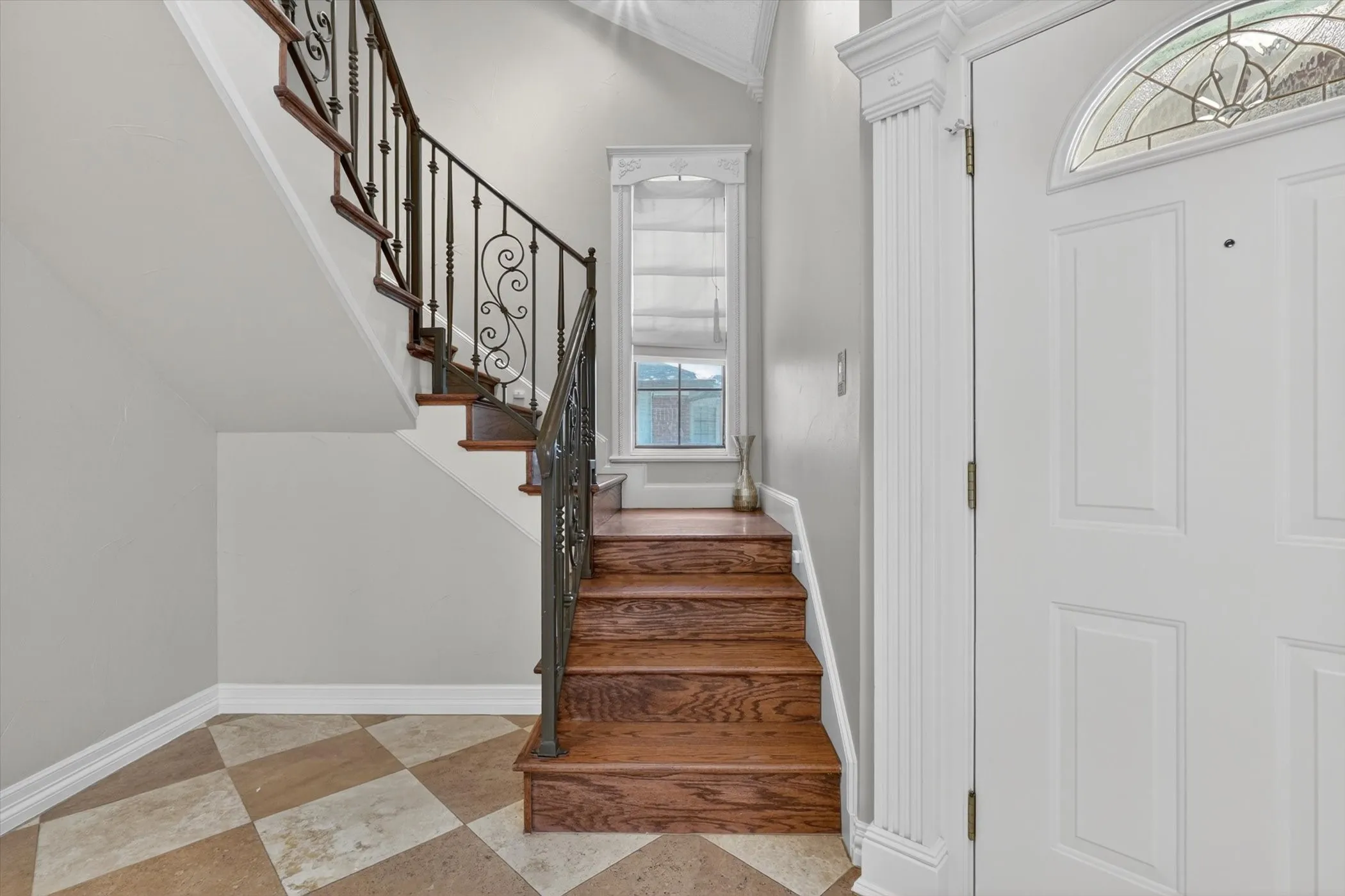 Entryway featuring a wood-finish staircase with wrought iron balusters, a leaded glass transom window, and checkered tile flooring