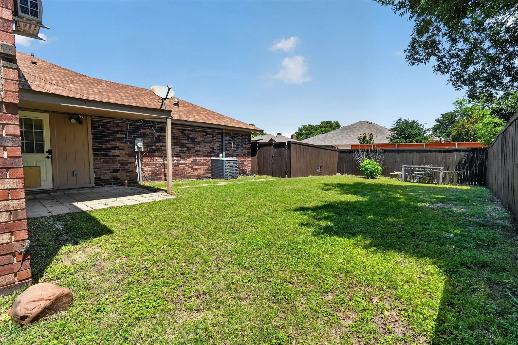 Expansive backyard featuring a lush lawn, privacy fencing, and a covered patio area with a paved surface