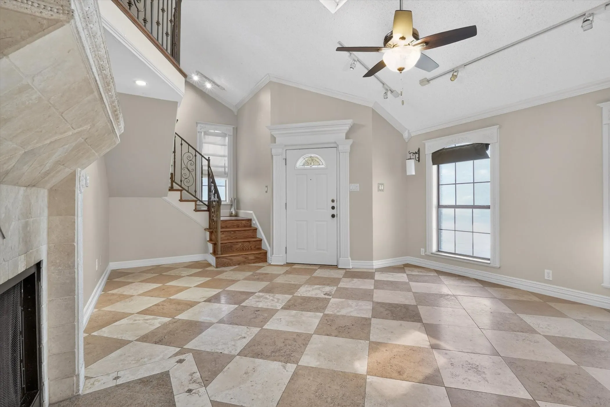 Spacious entry hall featuring checkerboard tile flooring, a staircase with wrought iron balusters, a built-in fireplace, vaulted ceilings, and a ceiling fan with integrated lighting