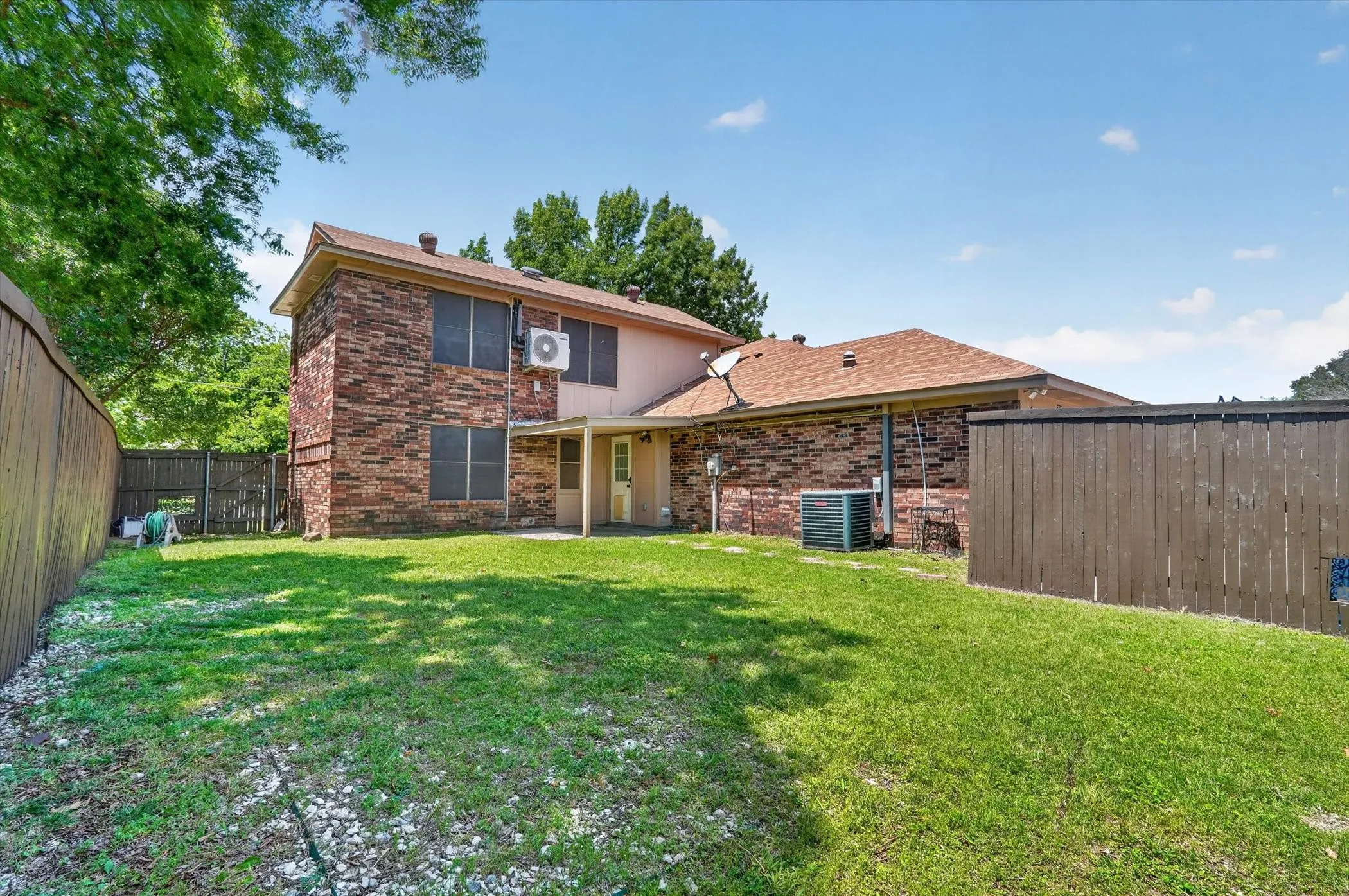 Expansive rear yard featuring a manicured lawn, full privacy fencing, and a covered patio area