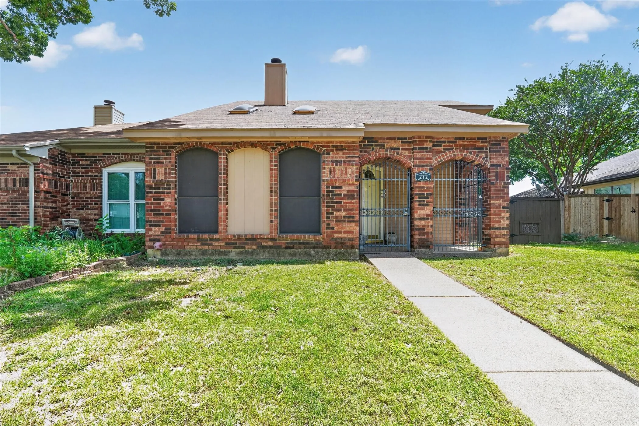 Brick exterior featuring arched window openings, a prominent front entry with security gate, and a concrete walkway