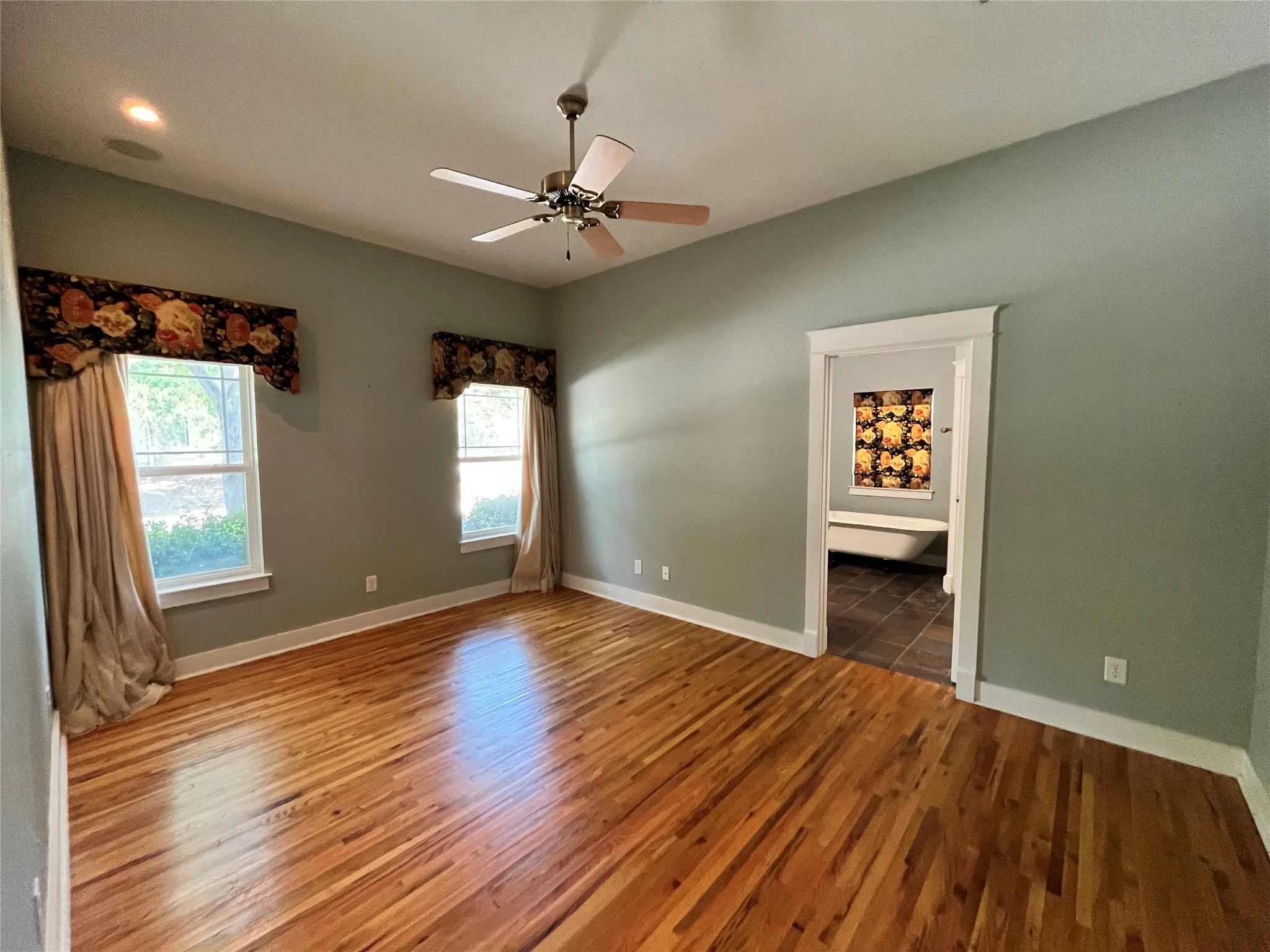 Large primary bedroom with hardwood floors and a ceiling fan.