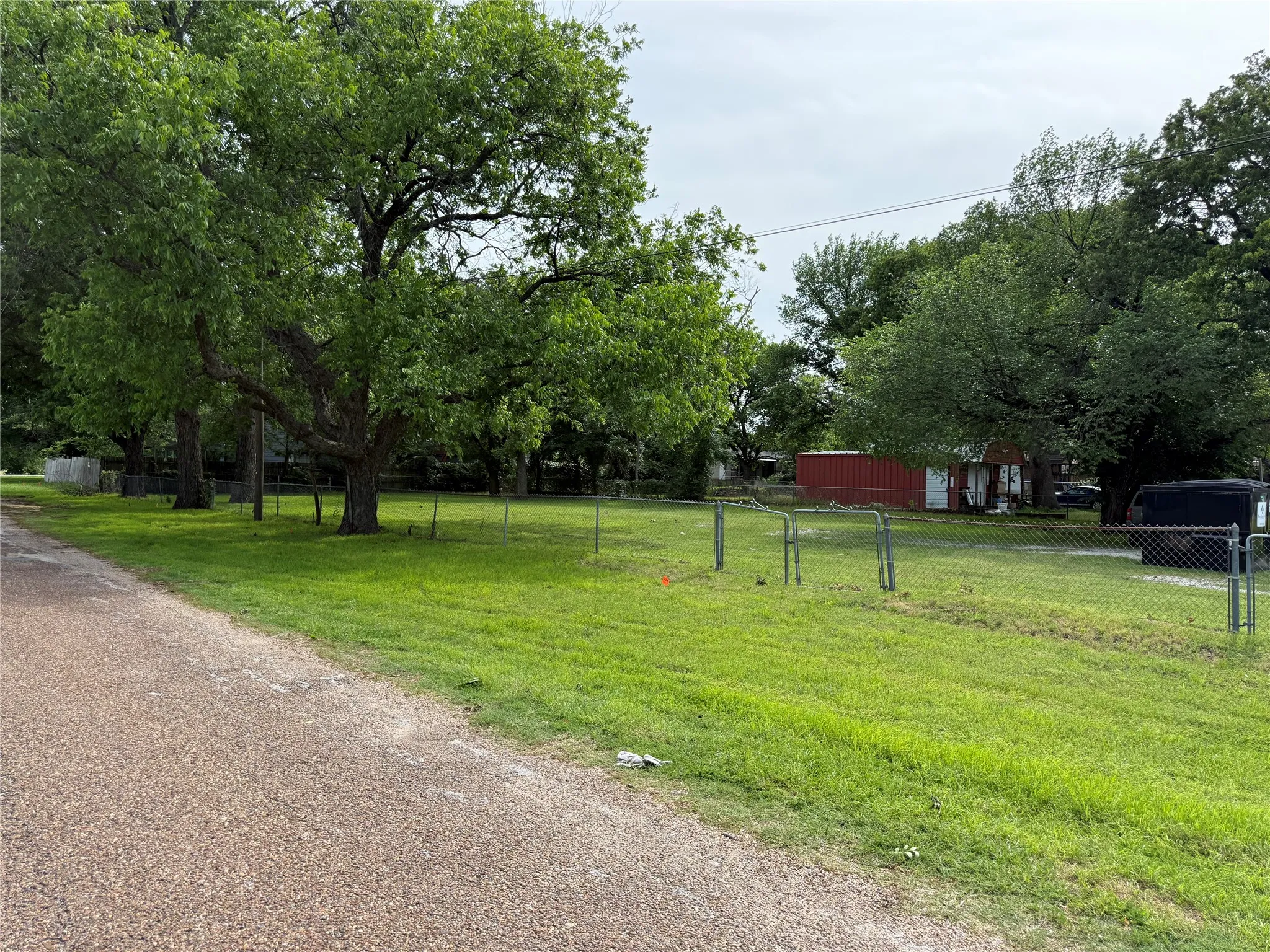 Expansive green lawn with mature trees and a chain-link fence