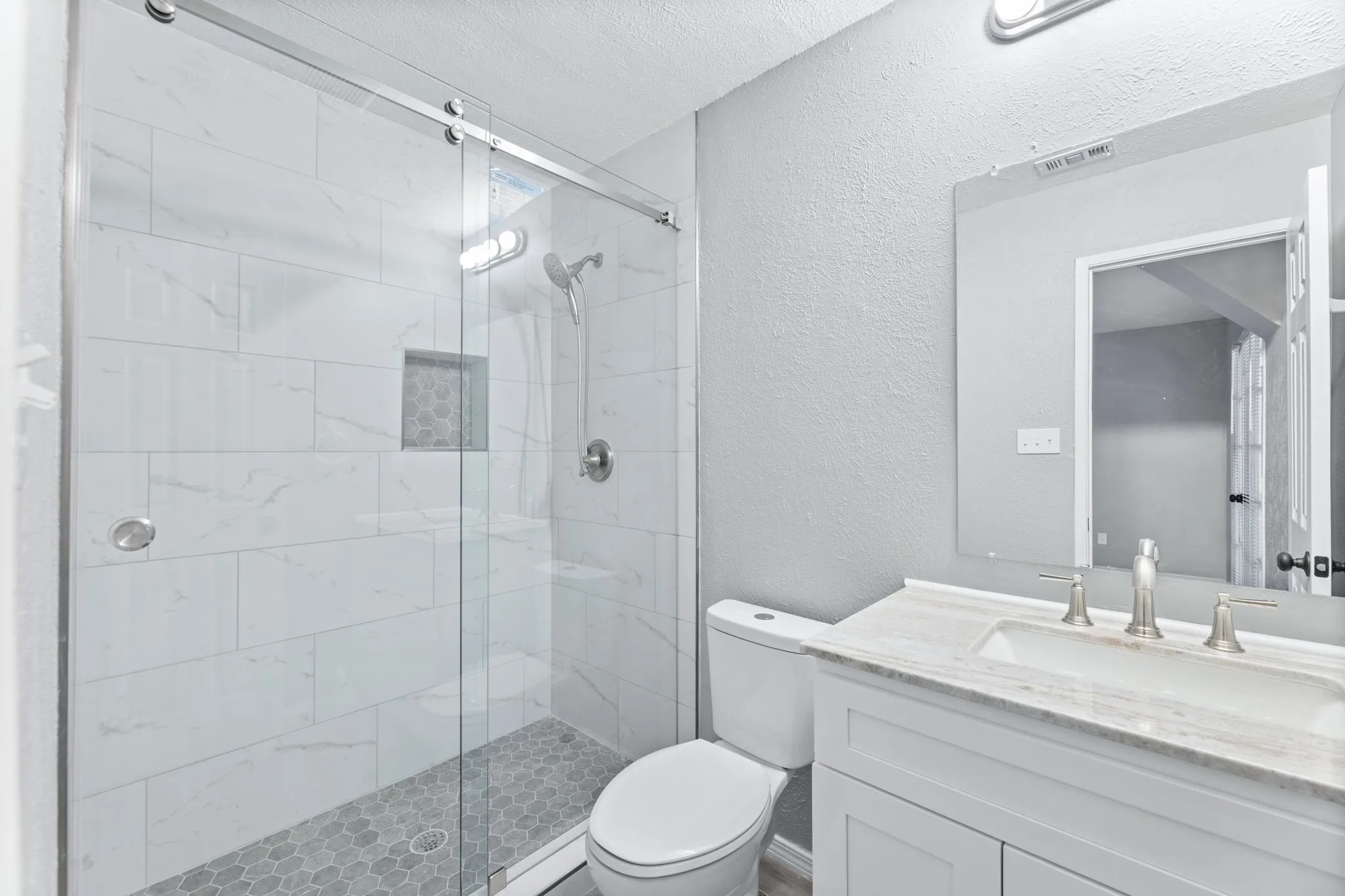 Primary Bathroom featuring a textured wall, a walk in shower, vanity, and a textured ceiling