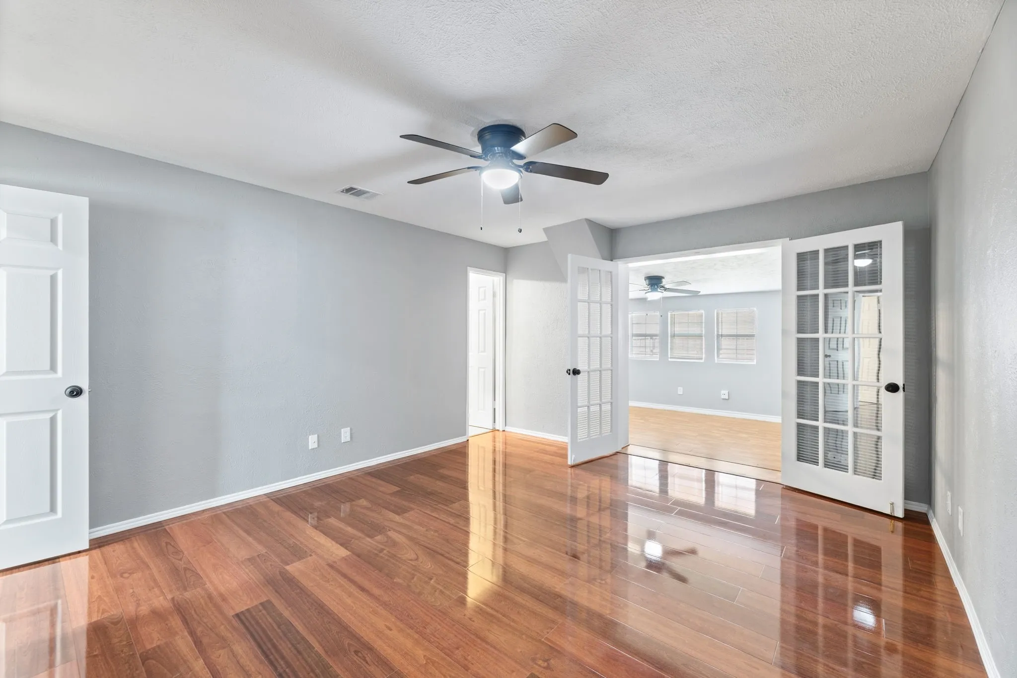 Primary bedroom, ensuite bath, french doors open to private office or sitting area. Featuring wood finished floors, a textured ceiling, and a ceiling fan & closet.