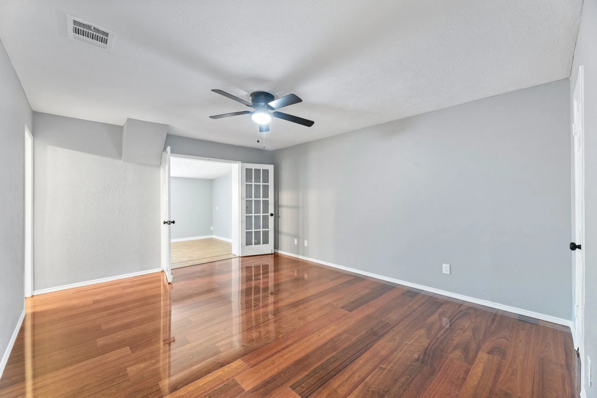 Another view of Primary bedroom, featuring wood finished floors, ceiling fan, and french doors