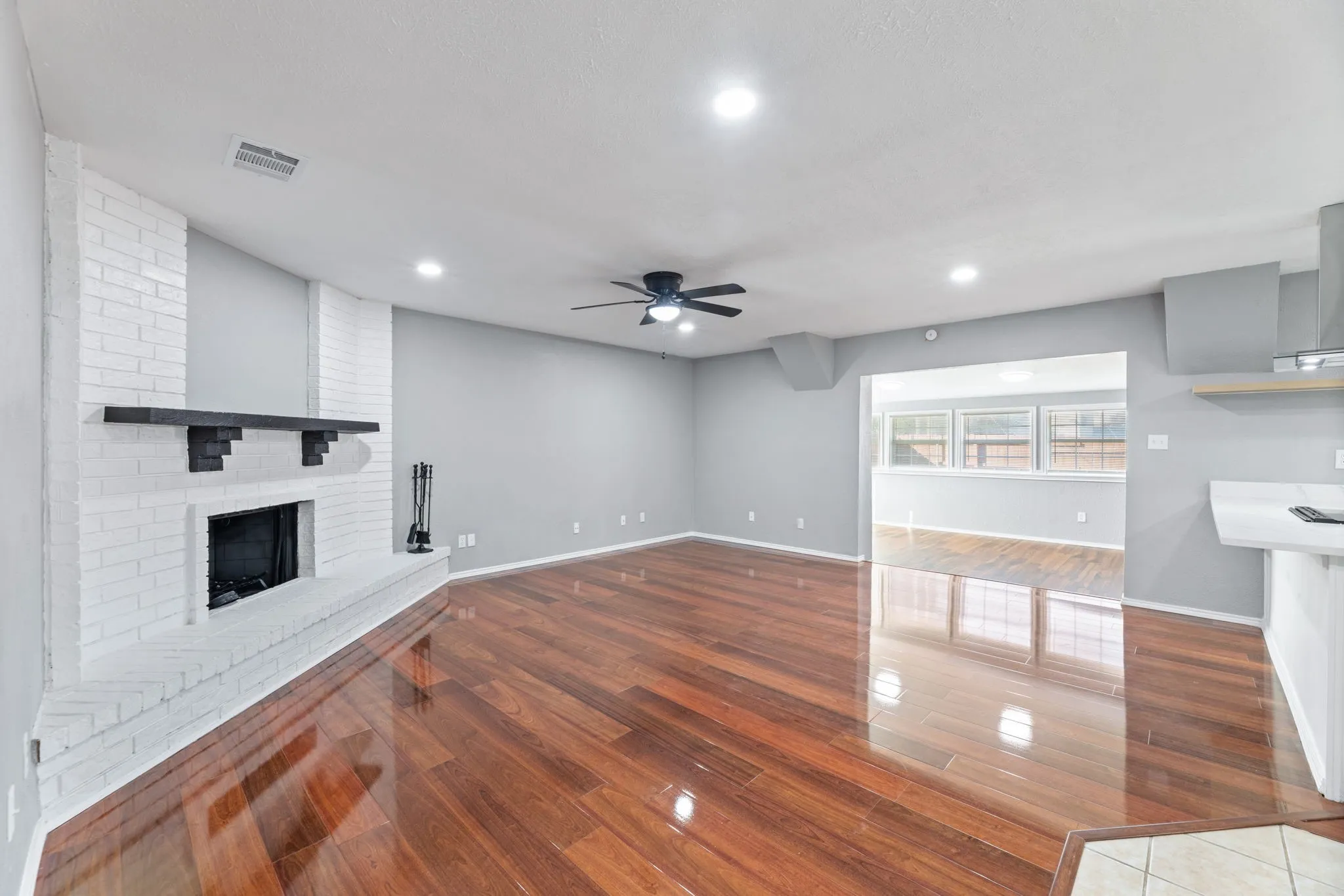 Unfurnished living room featuring wood finished floors, a brick fireplace, a ceiling fan, and recessed lighting