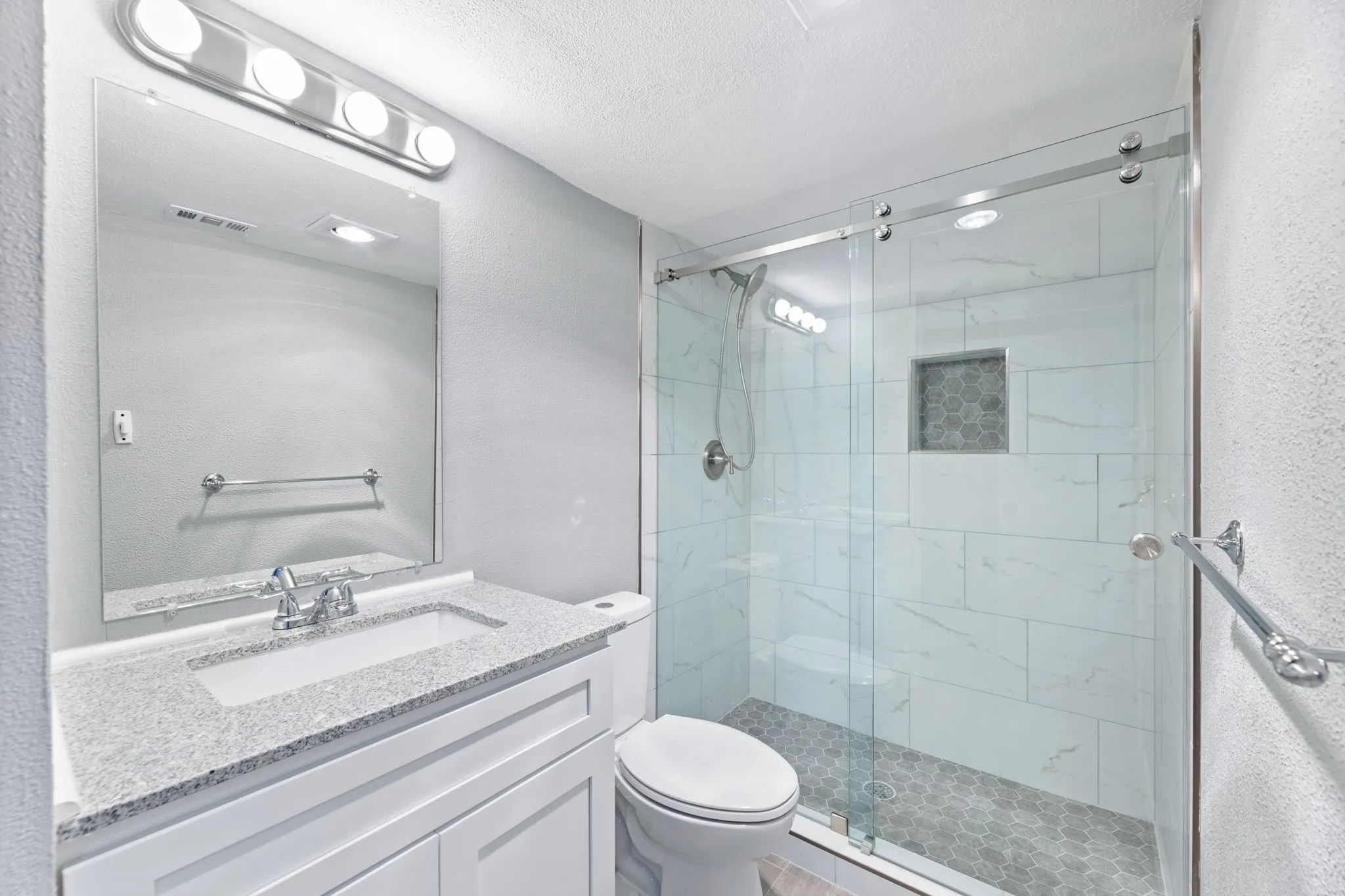 Second Full bathroom with a marble finish shower, a textured ceiling, vanity, and a textured wall