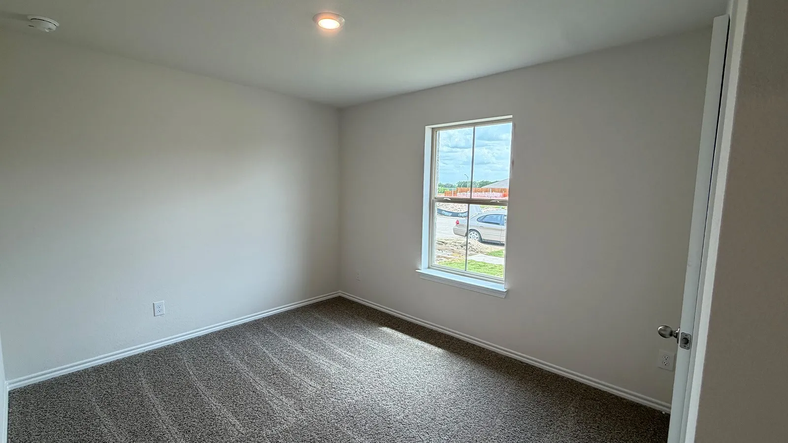 Bright interior room featuring a window with exterior views, neutral wall paint, gray carpet flooring, and white trim
