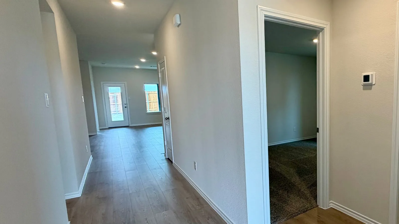 Hallway with wood-finish flooring, recessed lighting, and a white interior door leading to a room with dark carpeting