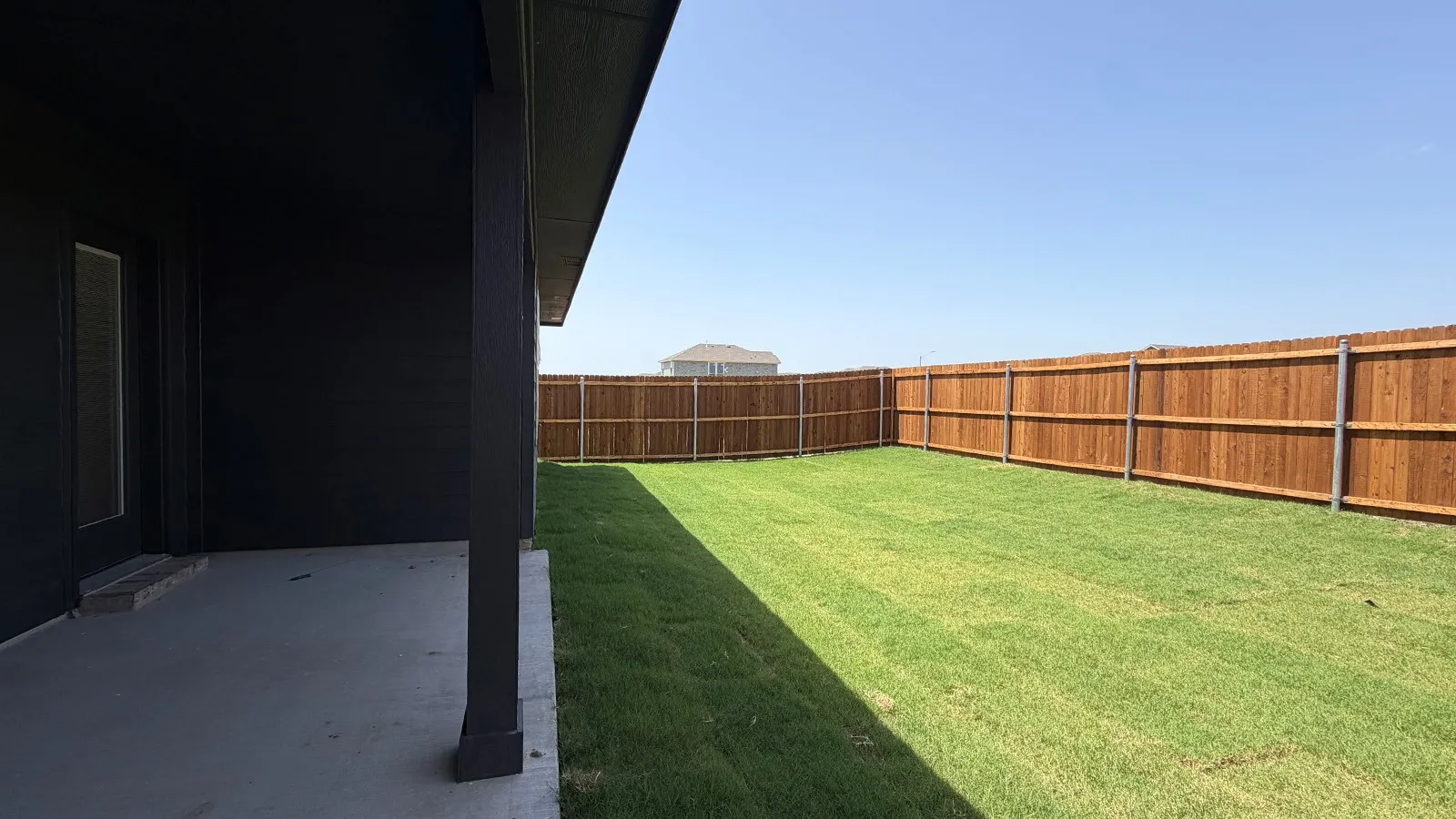 Expansive backyard featuring a manicured lawn, full perimeter privacy fencing, and a concrete patio with a covered section