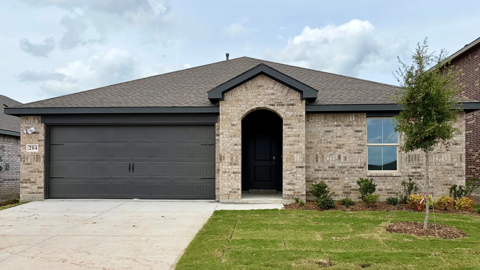 Brick facade home featuring an arched entryway, dark garage door, and a single front window