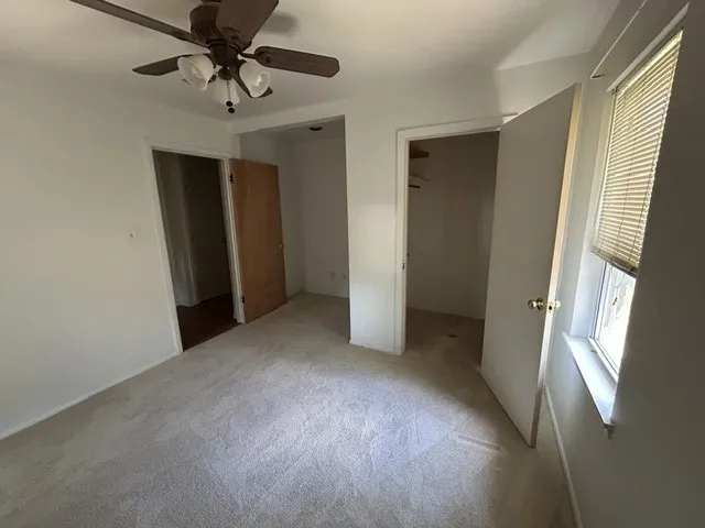 Carpeted room featuring a ceiling fan with integrated lighting, a window with blinds, and two doorways