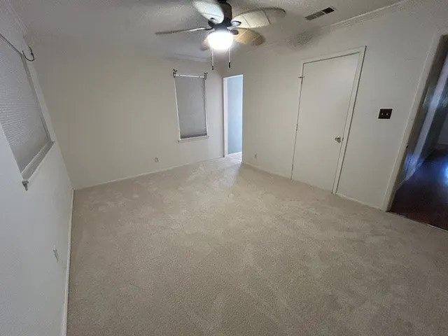 Carpeted interior space featuring neutral wall tones, a ceiling fan with integrated lighting, and white trim