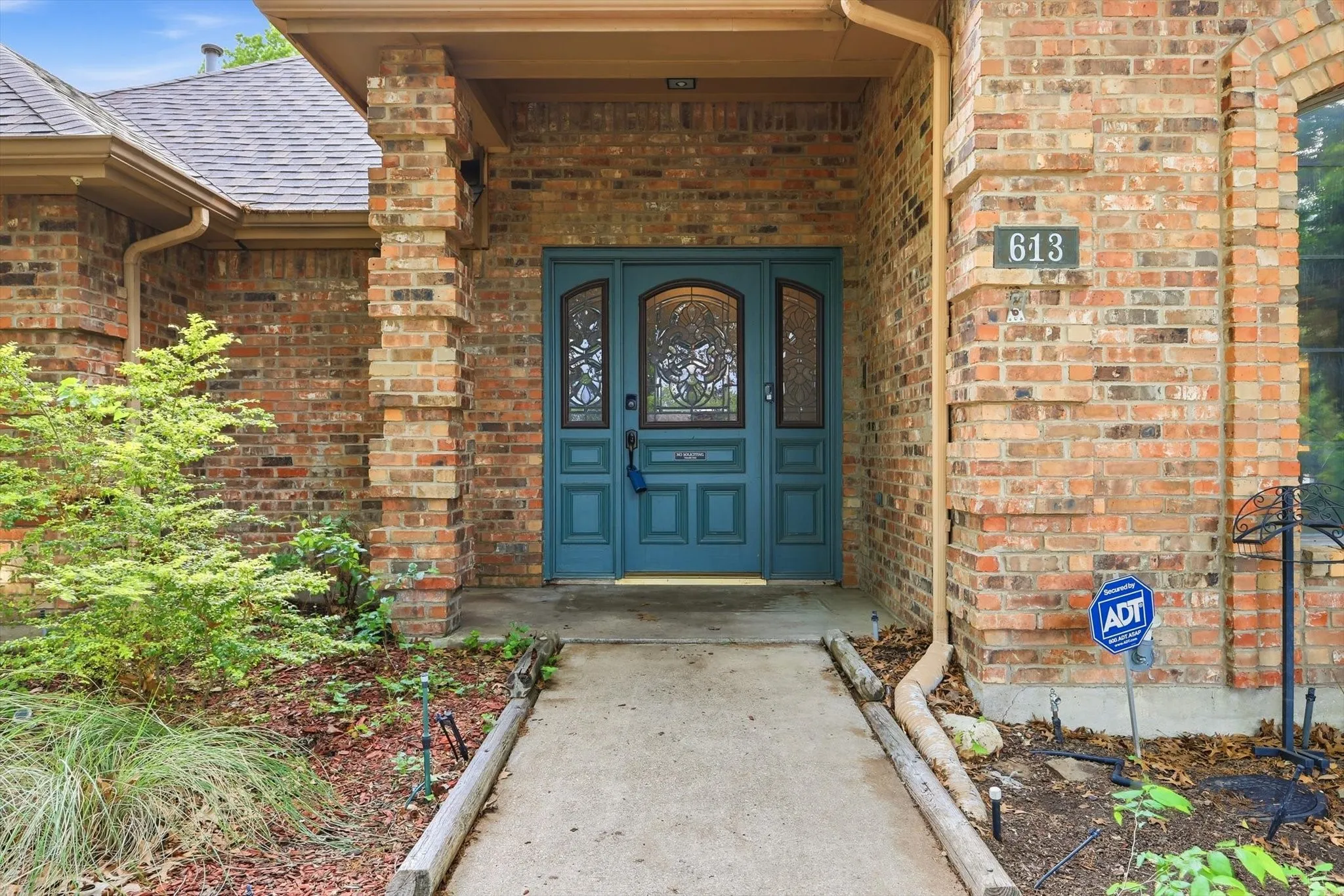 Brick exterior featuring a teal double-door entry with arched glass panels, flanked by sidelights