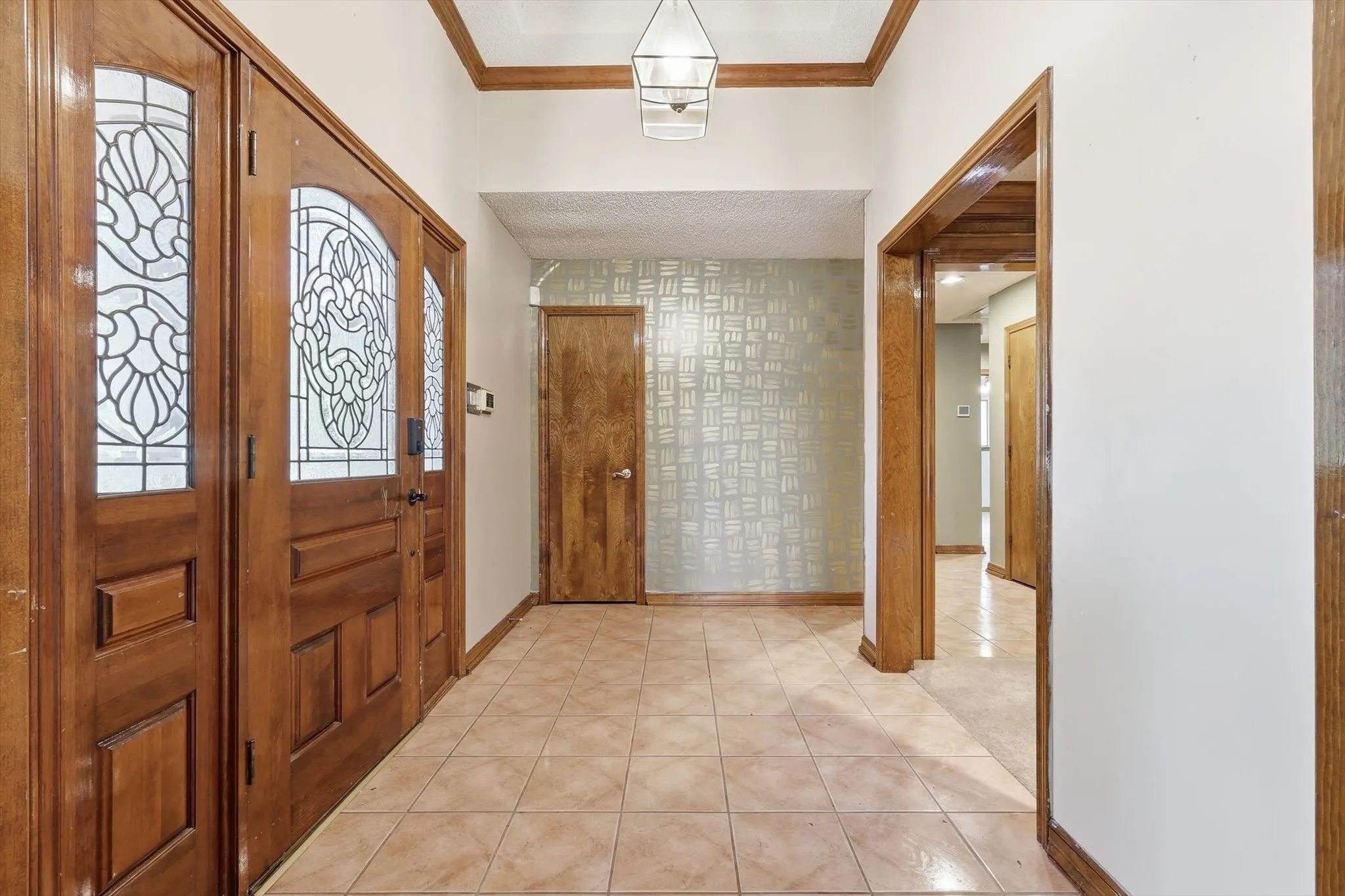 Entryway featuring decorative leaded glass double doors, tile flooring, wood trim, and a patterned accent wall