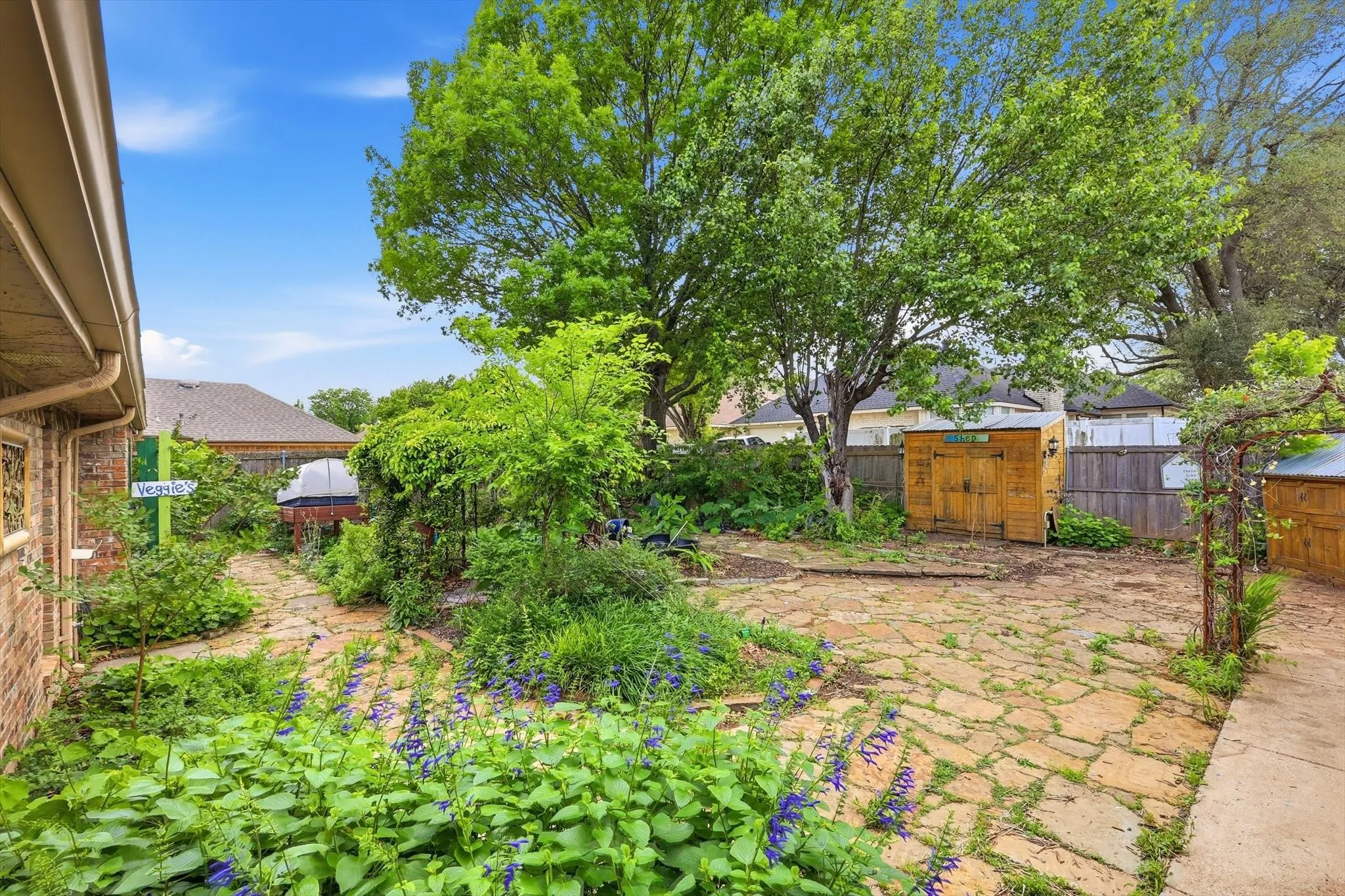 Expansive backyard featuring a natural stone patio, mature trees, and established garden beds with flowering plants