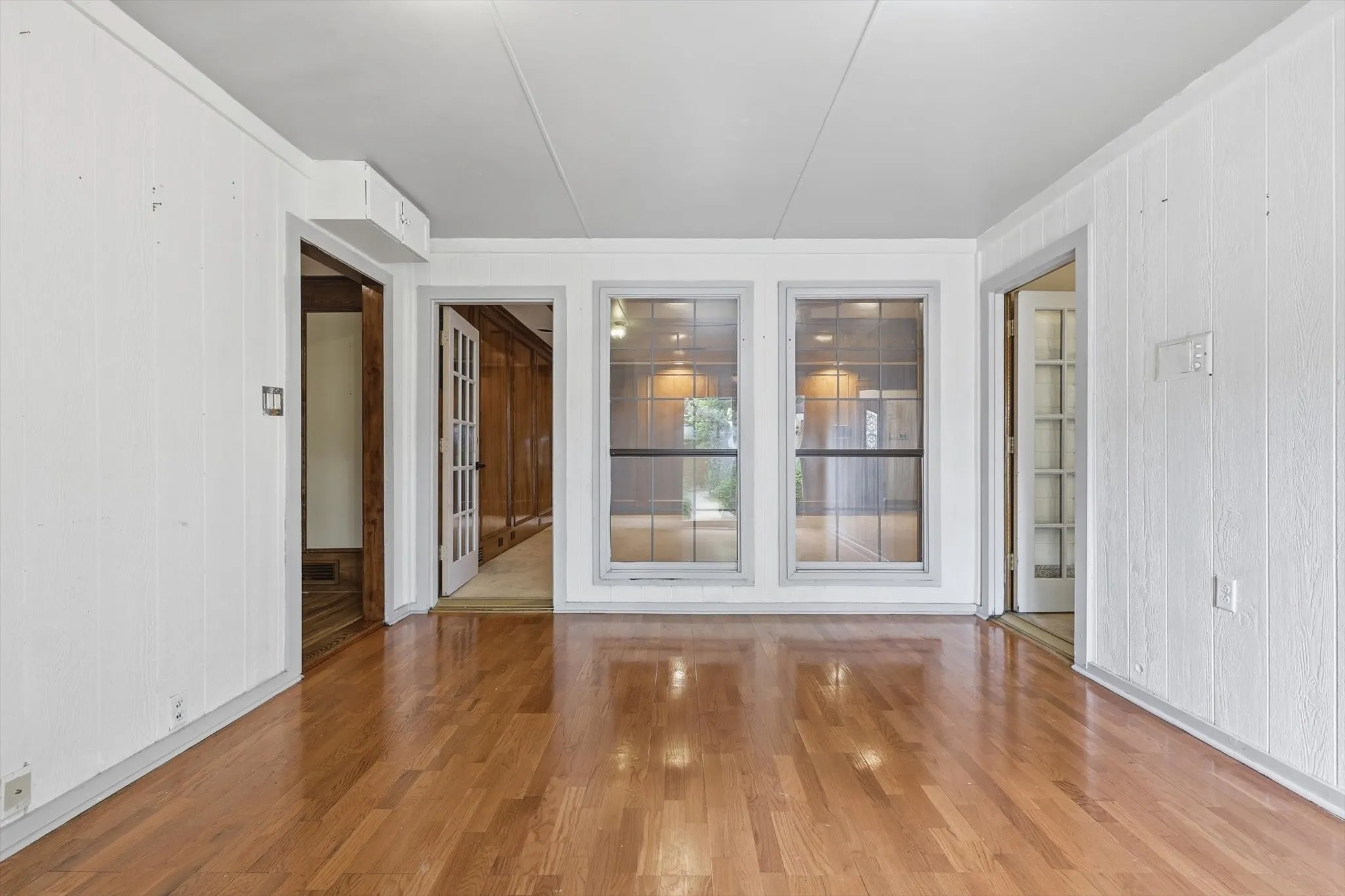 Spacious room featuring wood-finish flooring, white paneled walls, and two large windows