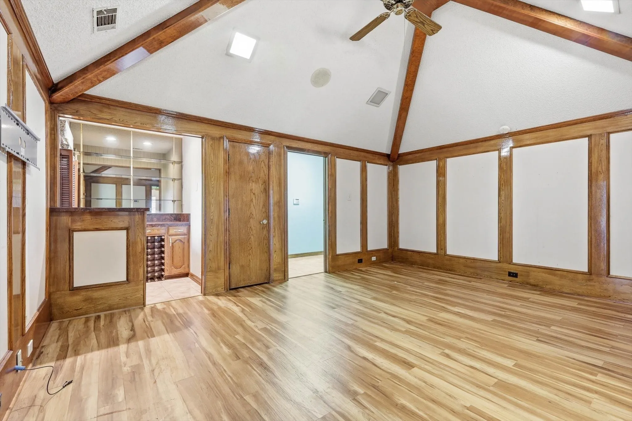 Spacious room featuring vaulted ceilings with exposed wood beams, wood-finish flooring, and a built-in wet bar with wine storage