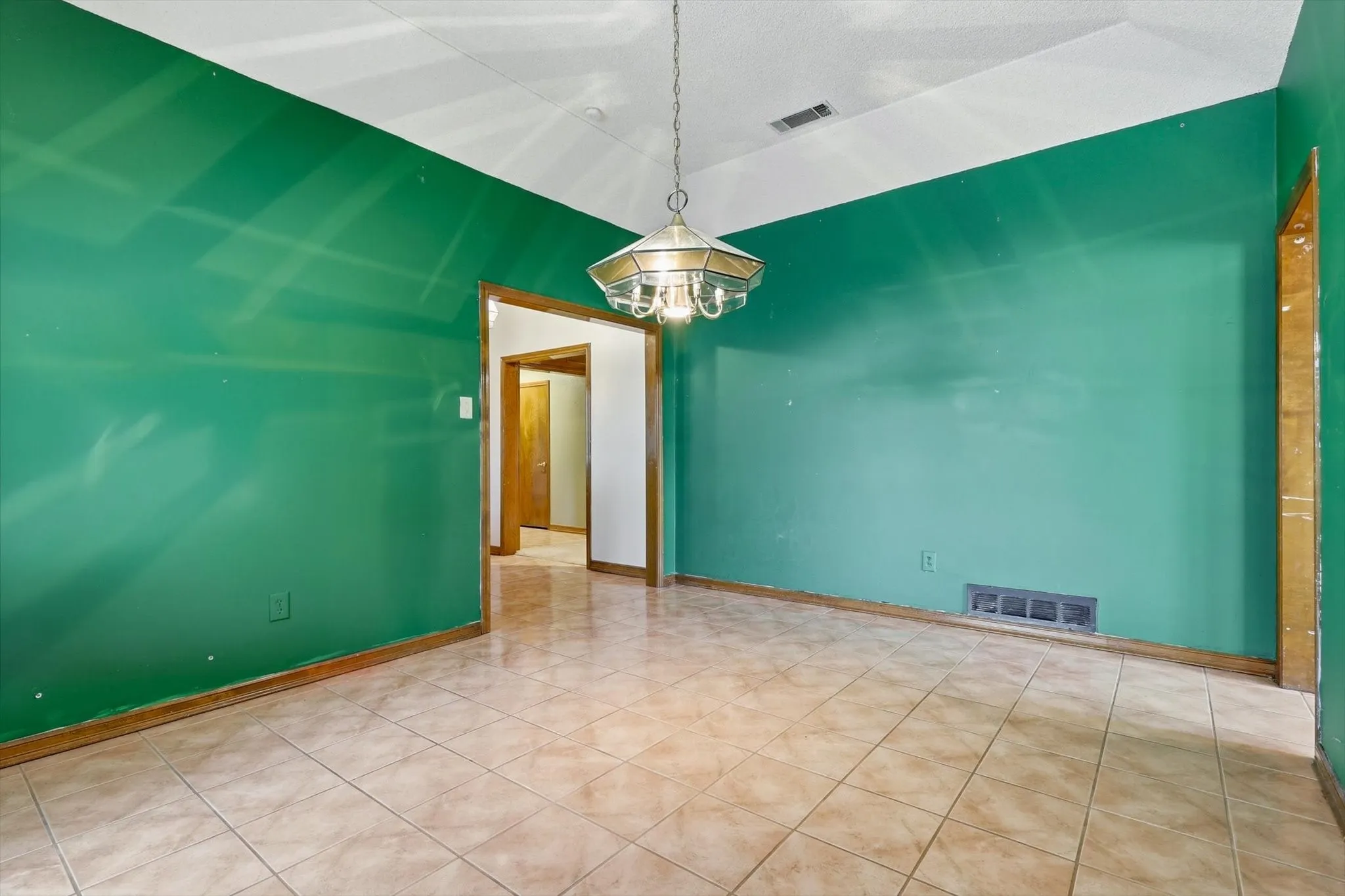 Open interior space featuring tiled flooring, a suspended chandelier, and a white ceiling with a visible vent