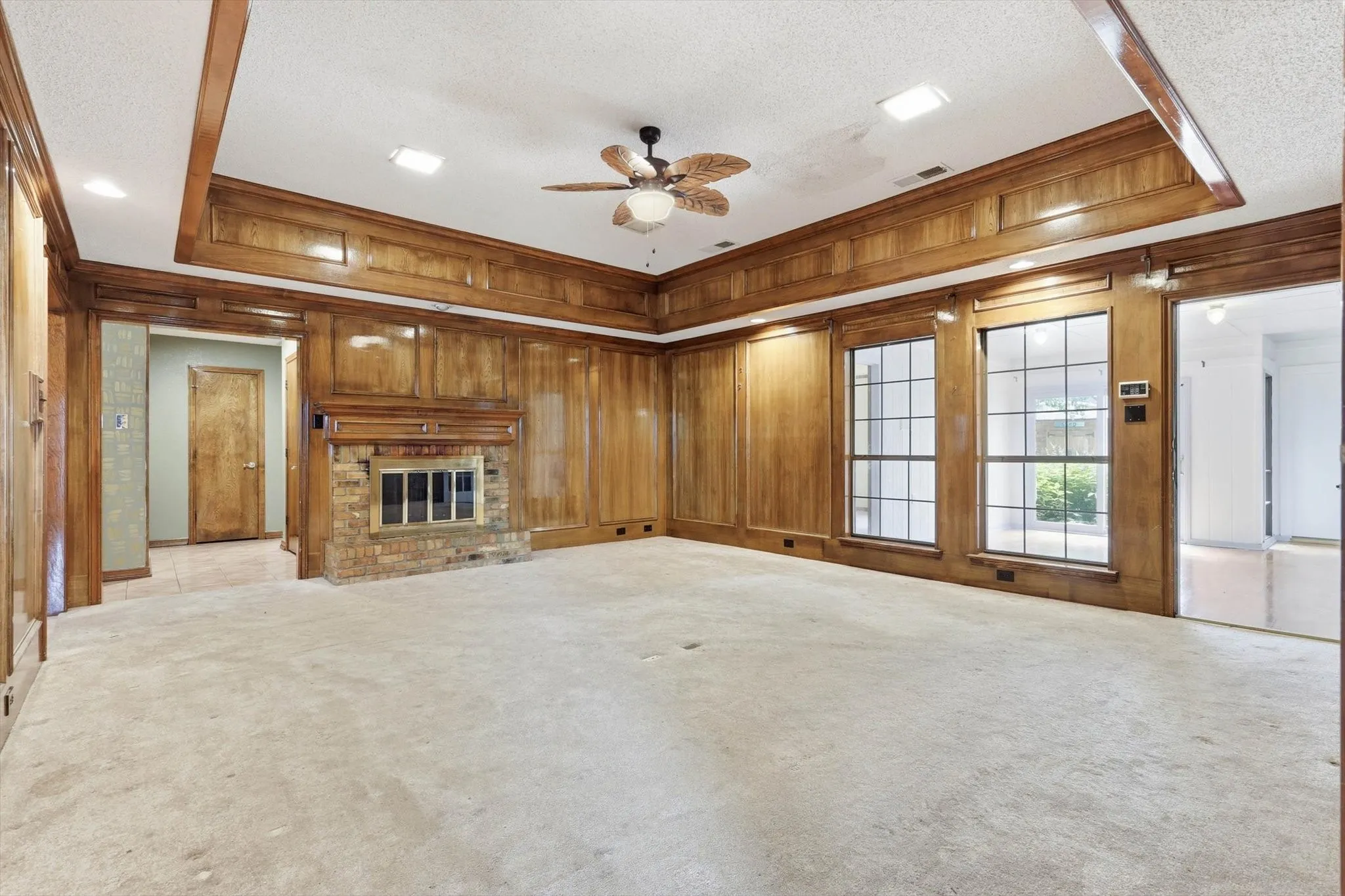 Spacious interior room featuring extensive wood paneling, a brick fireplace with a wood mantle, and a tray ceiling