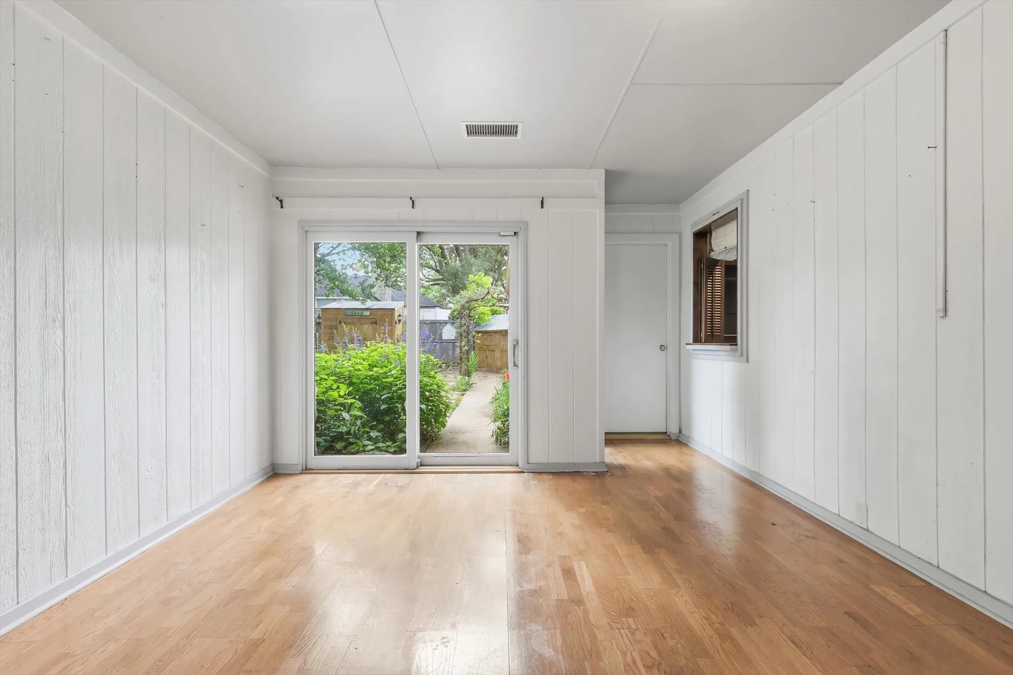 Interior space with wood-finish flooring, white vertical plank walls, and a sliding glass door