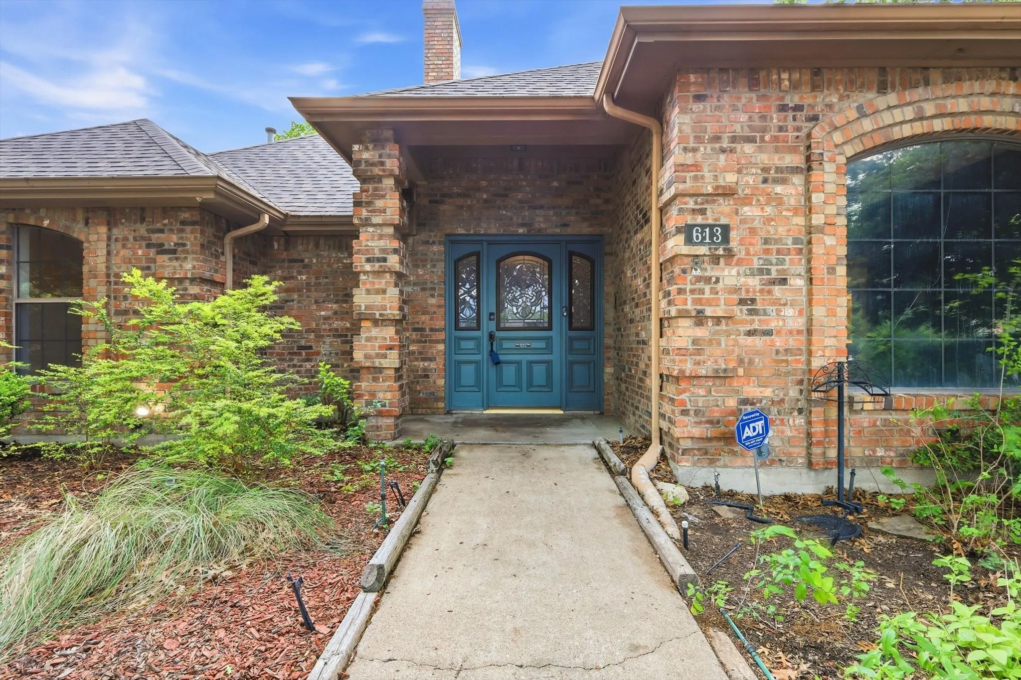 Brick exterior featuring a teal double entry door with decorative glass, an arched window, and a concrete walkway