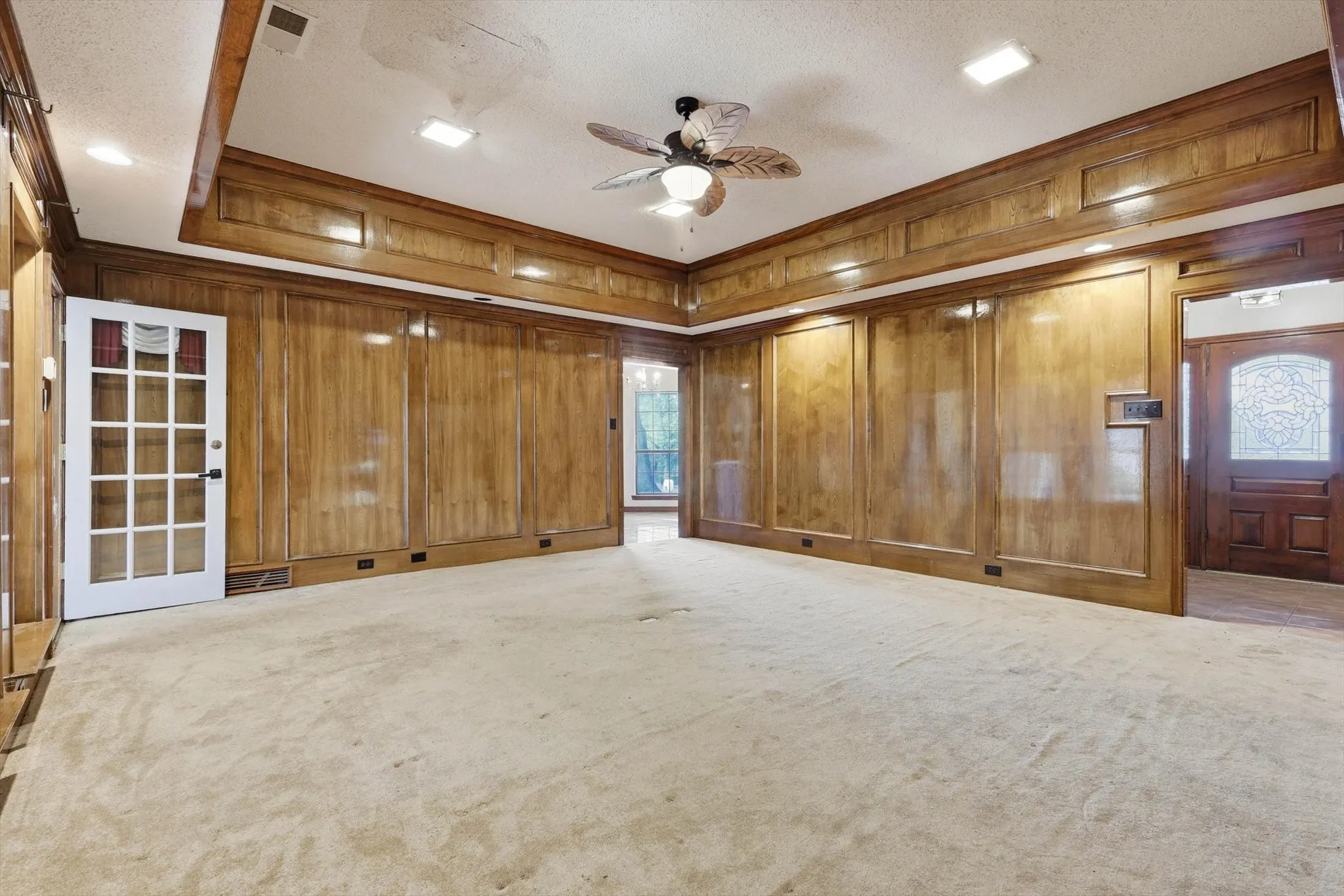 Room featuring extensive wood paneling, a tray ceiling with recessed lighting, and a decorative ceiling fan