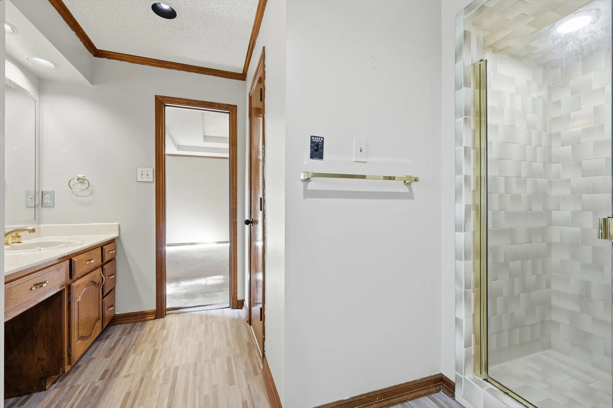 Bathroom featuring a glass-enclosed shower with geometric tile, a wood-finish vanity with an integrated sink, and wood-finish flooring