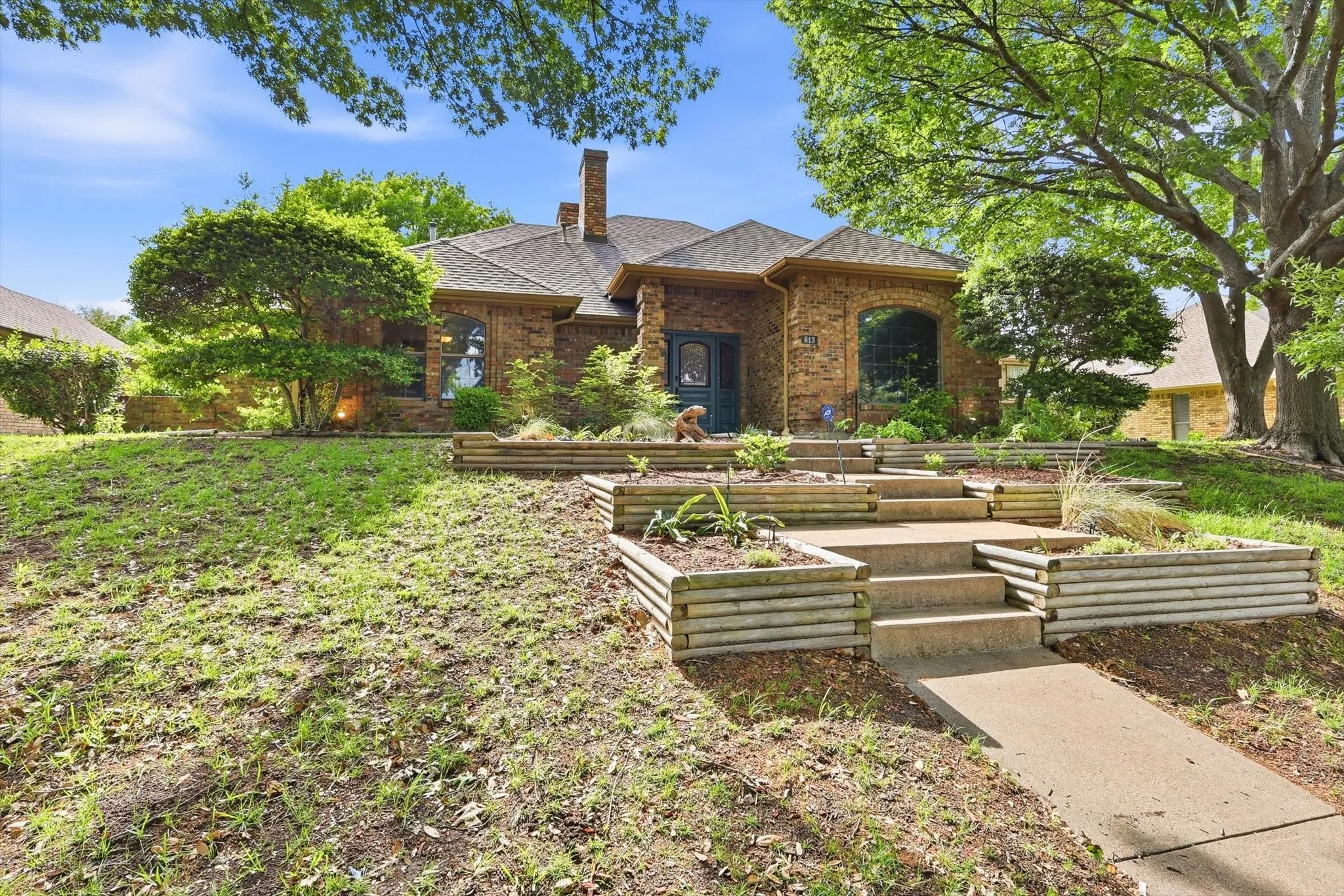 Brick exterior residence featuring a stepped concrete walkway, tiered planter beds, and mature landscaping