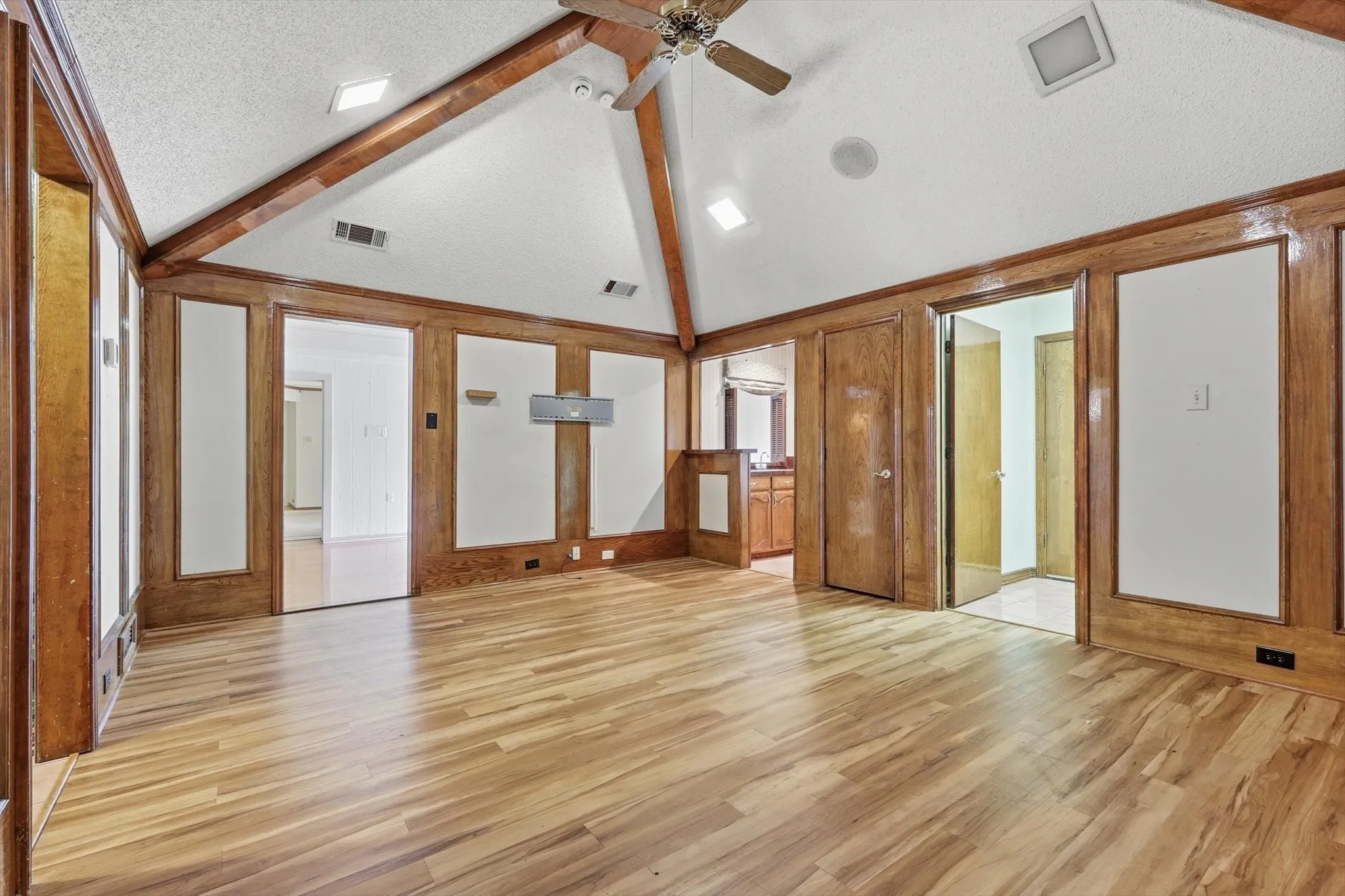 Spacious interior featuring a vaulted ceiling with exposed wood beams, wood-finish flooring, and extensive wood paneling