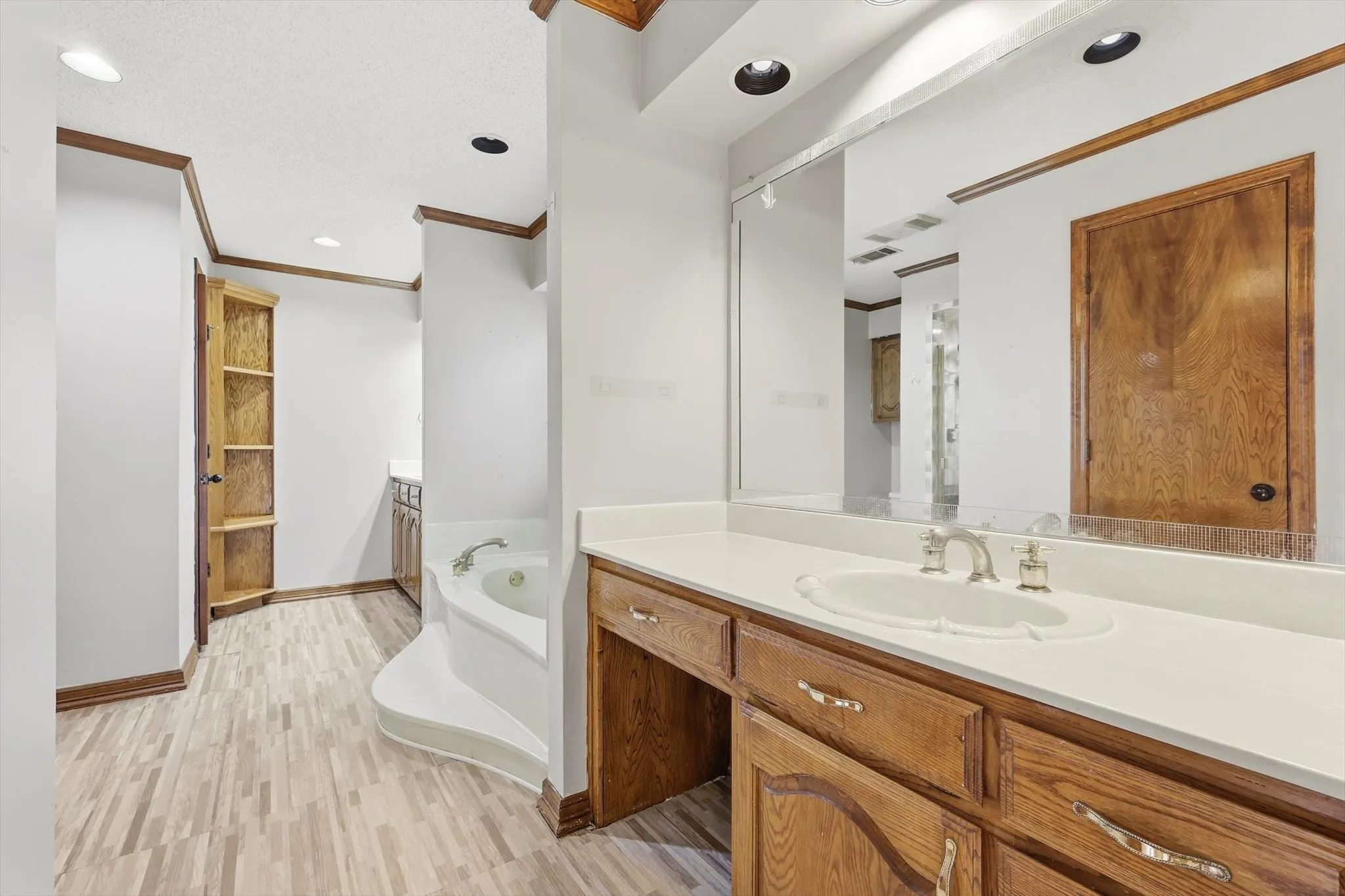 Bathroom featuring a built-in jetted tub, wood-finish flooring, wood cabinetry with a vanity area, and recessed lighting