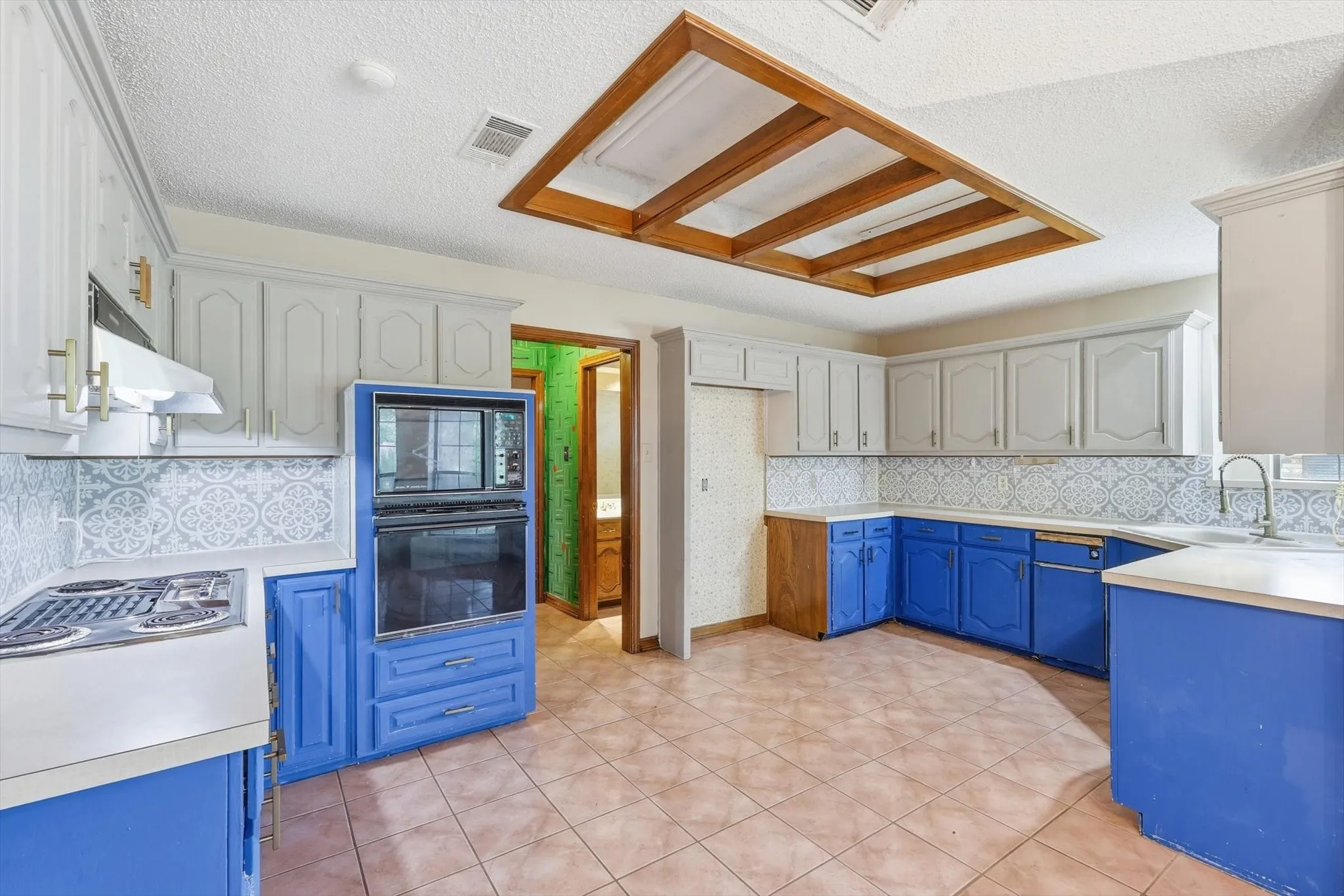 Kitchen featuring blue and white cabinetry, a built-in oven and microwave, patterned backsplash, tile flooring, and a decorative ceiling fixture