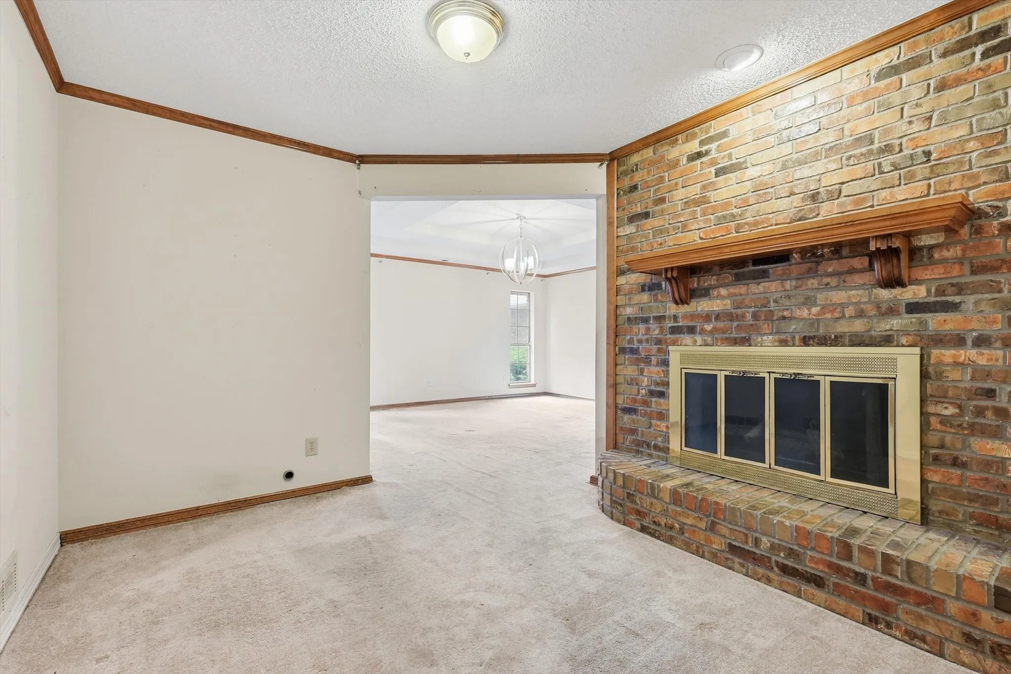 Brick fireplace with a wood mantle, carpet flooring, white walls, and wood trim