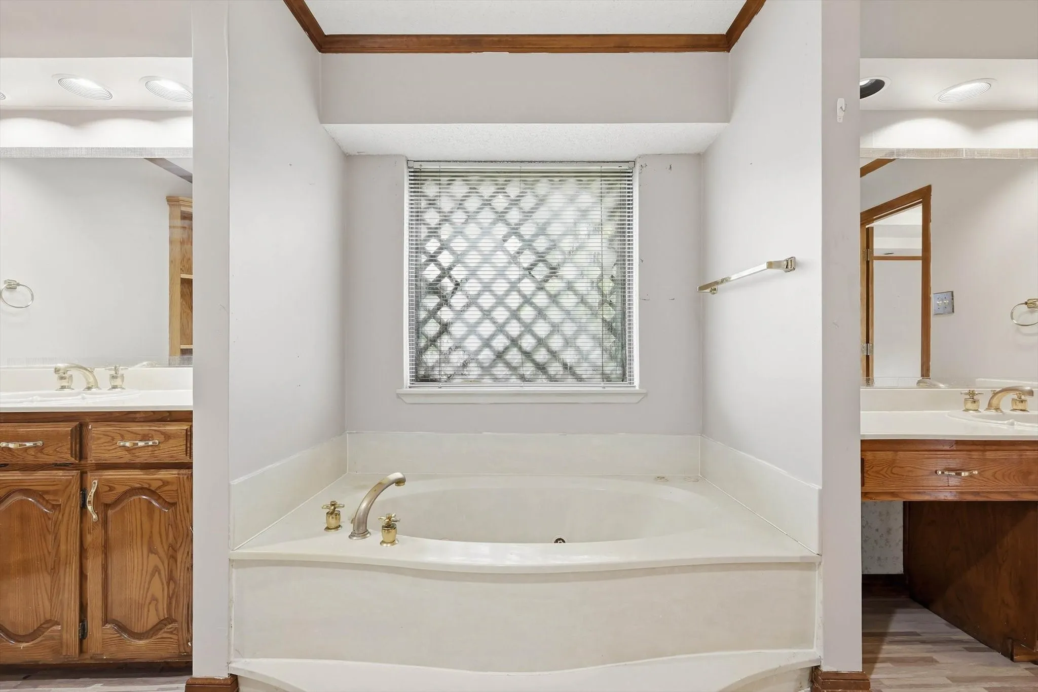 Built-in soaking tub with brass-finish fixtures, flanked by matching wood-finish vanities featuring integrated sinks and brass-finish faucets