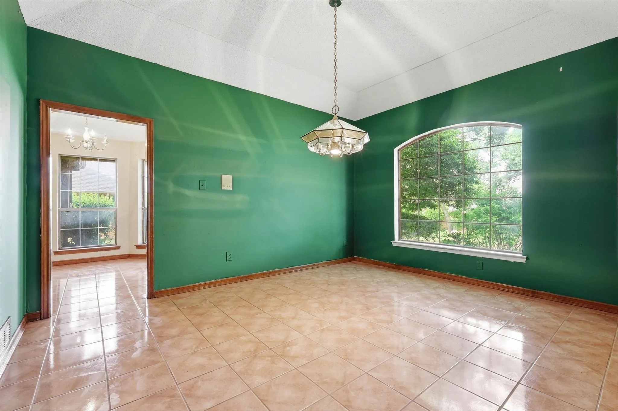 Room featuring an arched window with grid-pane detailing, a brass and glass chandelier, and a wide cased opening