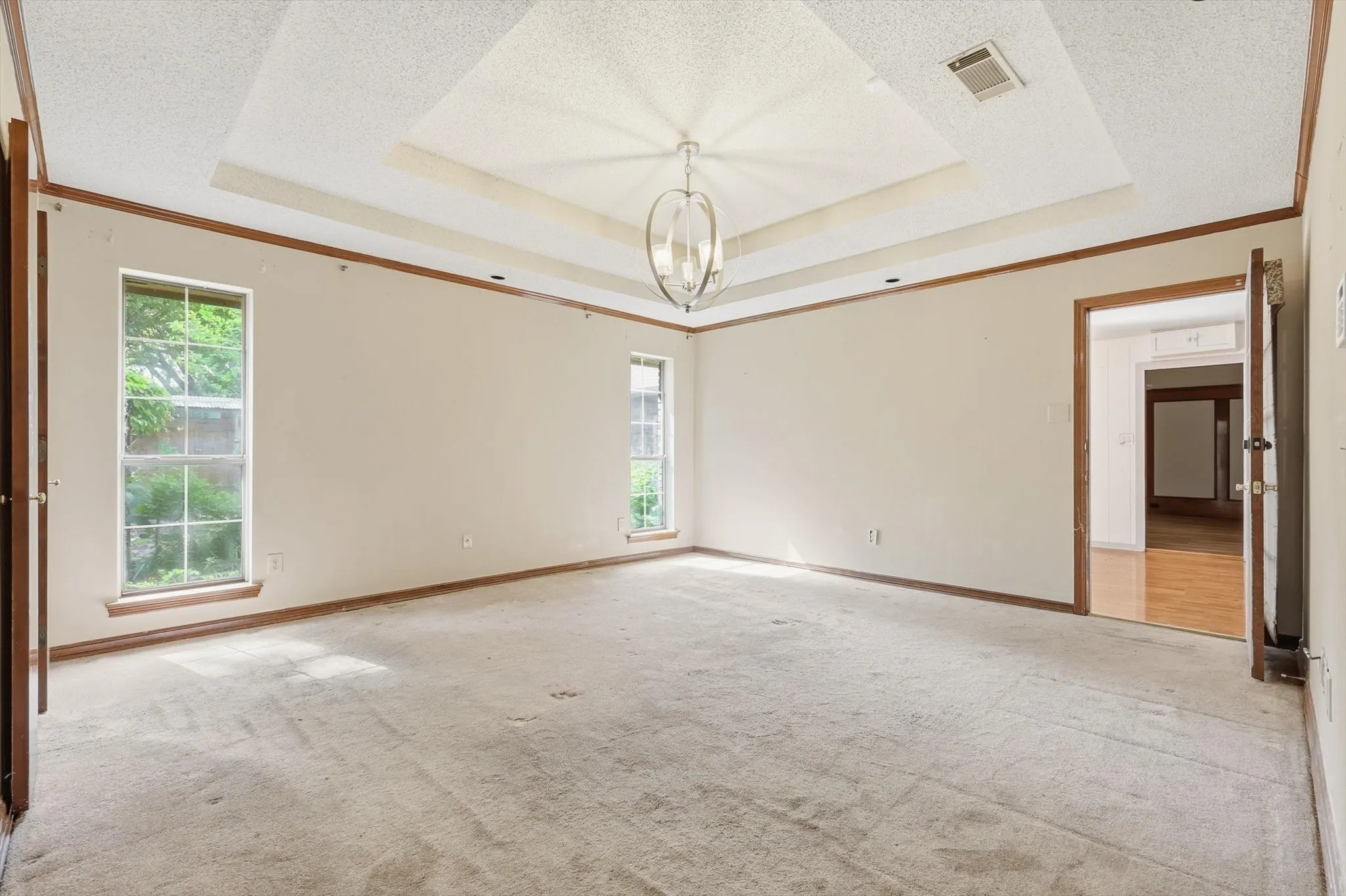 Spacious room featuring a tiered ceiling with a central light fixture, two tall windows, and wood-finish trim
