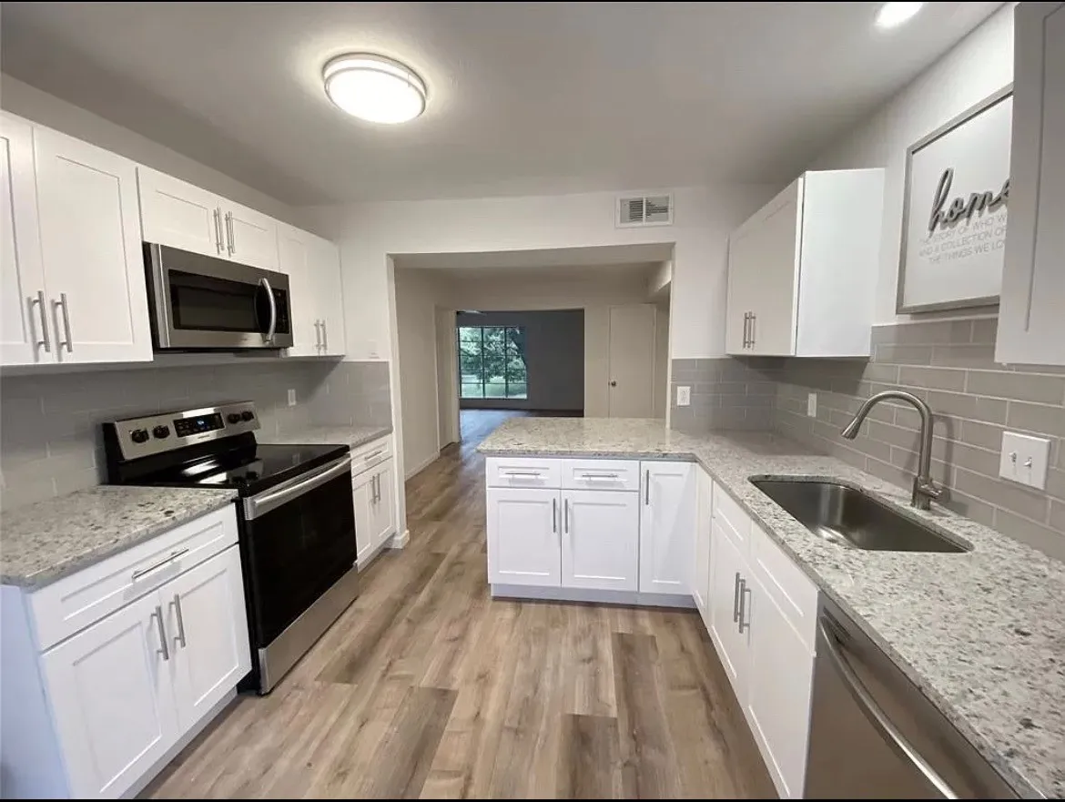 Contemporary kitchen featuring white cabinetry with brushed nickel hardware, light-toned countertops, subway tile backsplash, and wood-finish flooring