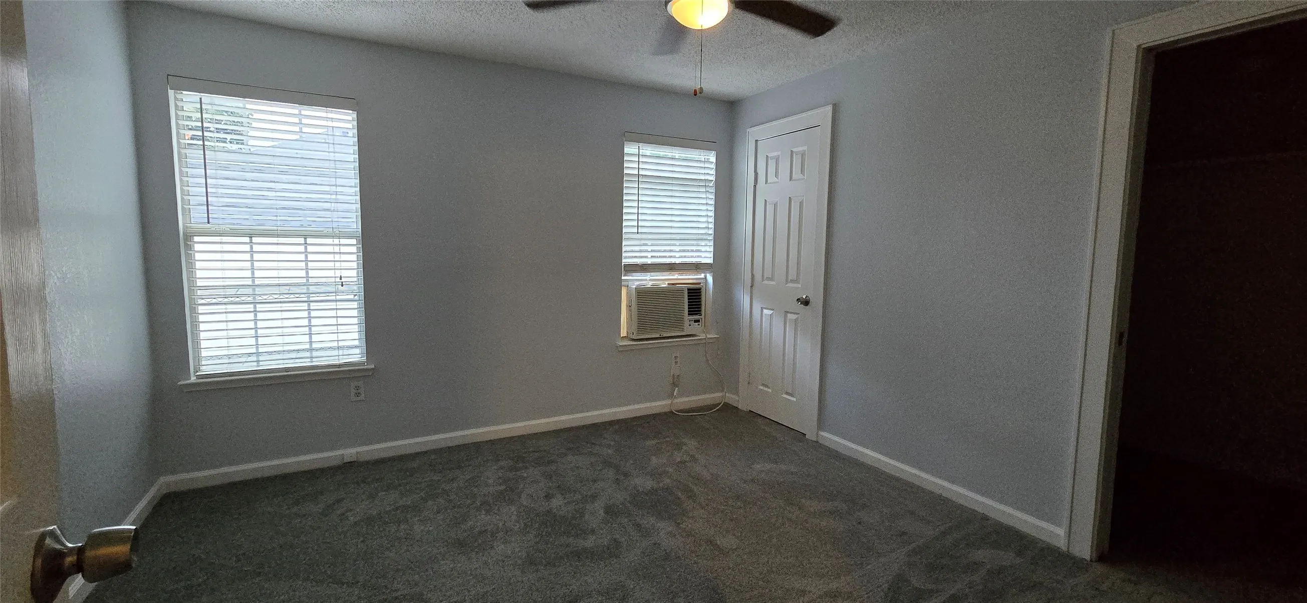 Unfurnished bedroom featuring a textured ceiling, dark carpet, a closet, cooling unit, and ceiling fan