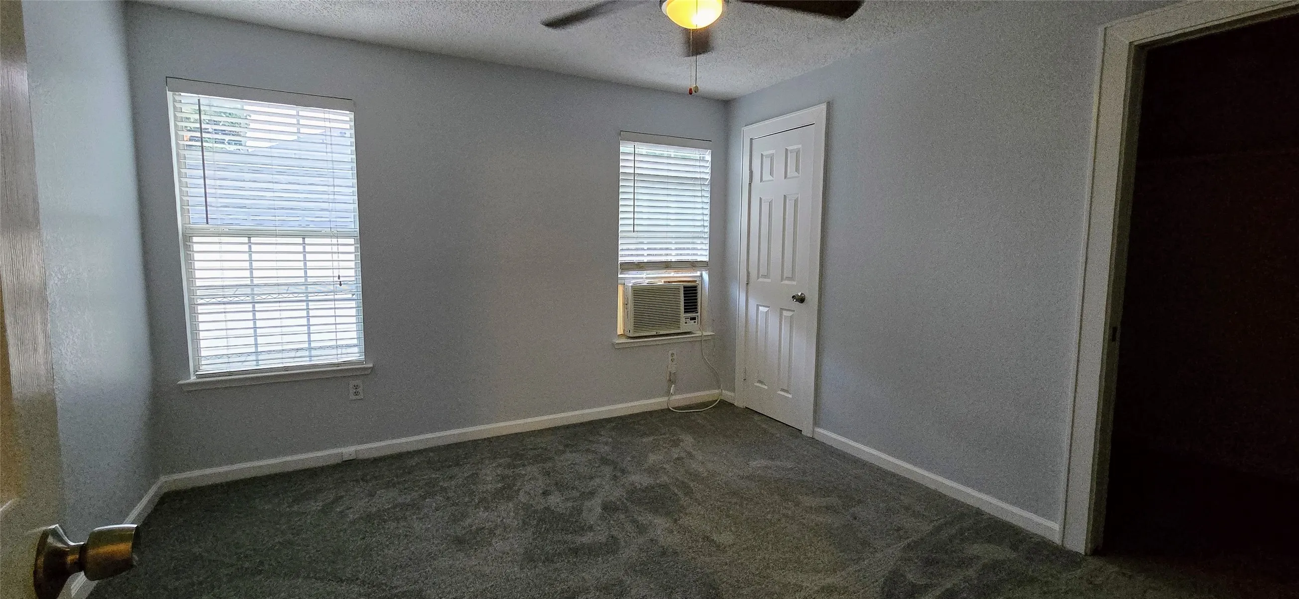 Unfurnished bedroom featuring ceiling fan, cooling unit, a textured ceiling, dark carpet, and a closet