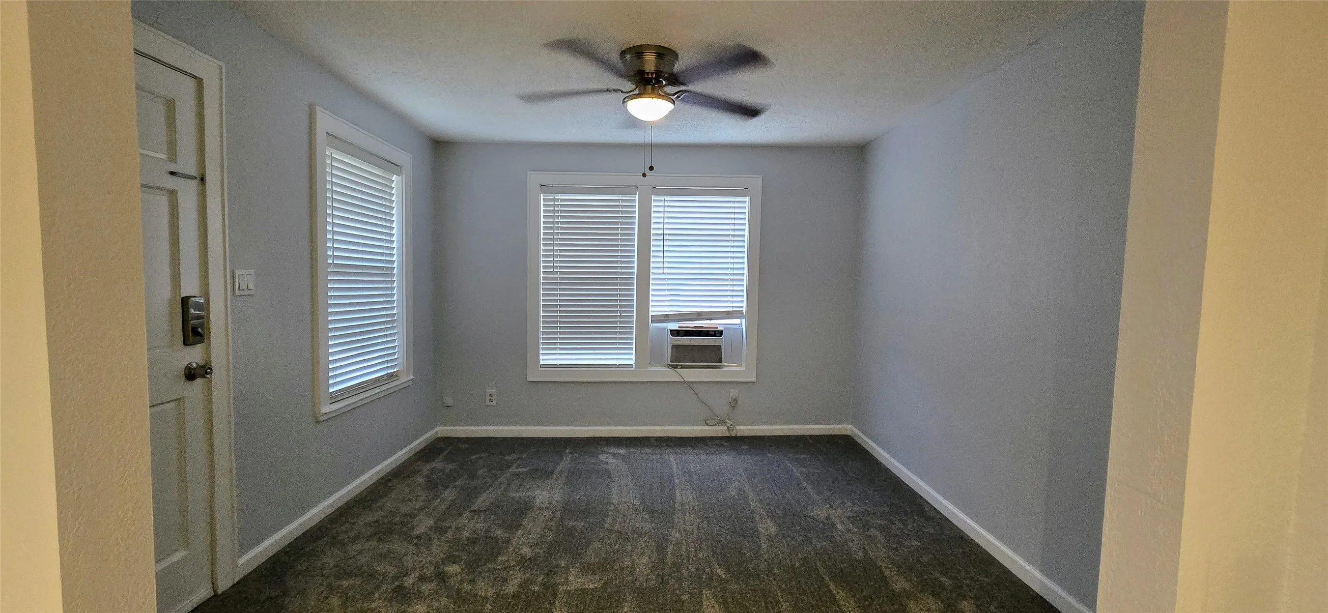 Unfurnished room featuring ceiling fan, dark carpet, and a wealth of natural light