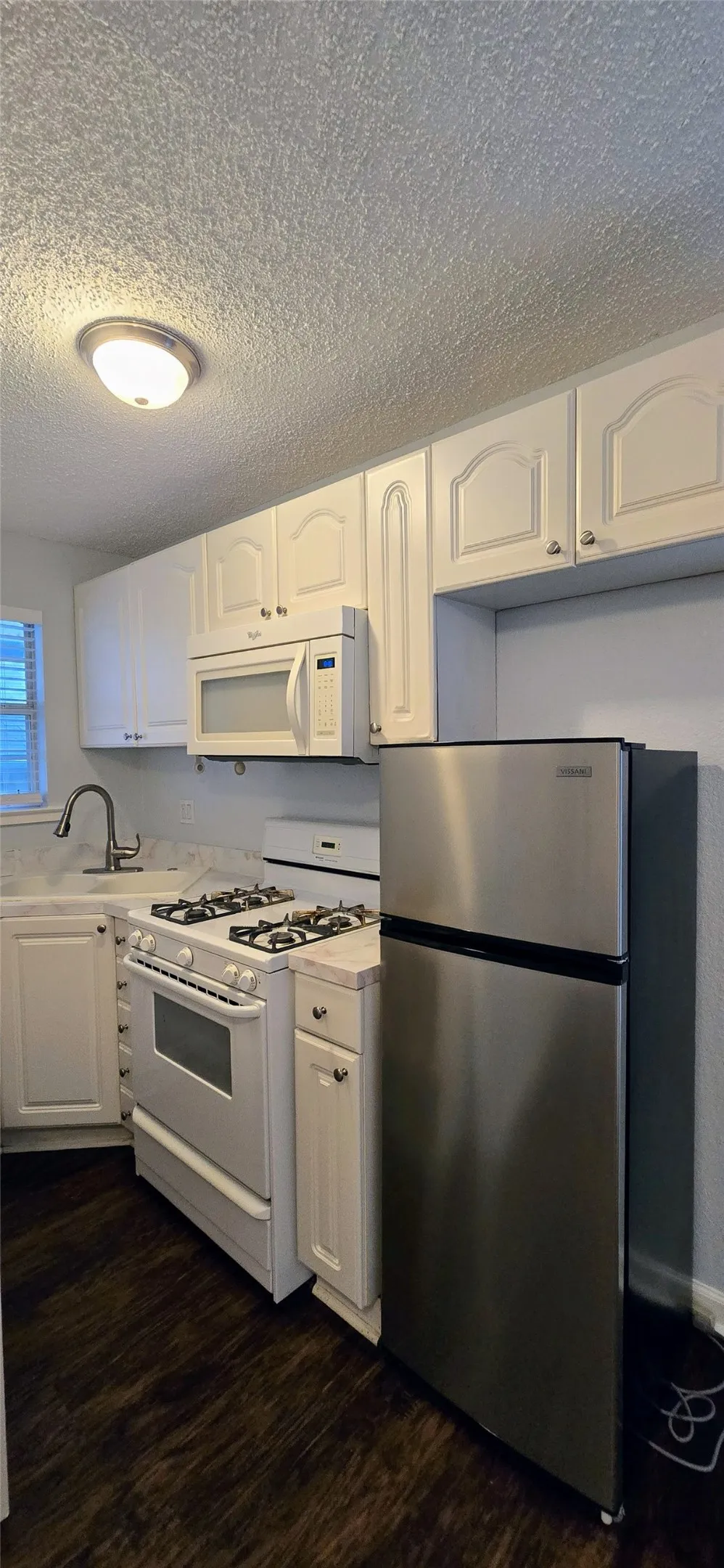 Kitchen featuring sink, a textured ceiling, dark hardwood / wood-style flooring, white appliances, and white cabinets