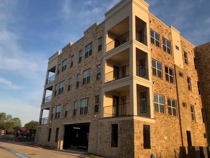 The property features a multi-story building with brick and stone cladding, balconies with black railings, and an integrated parking area on the ground level