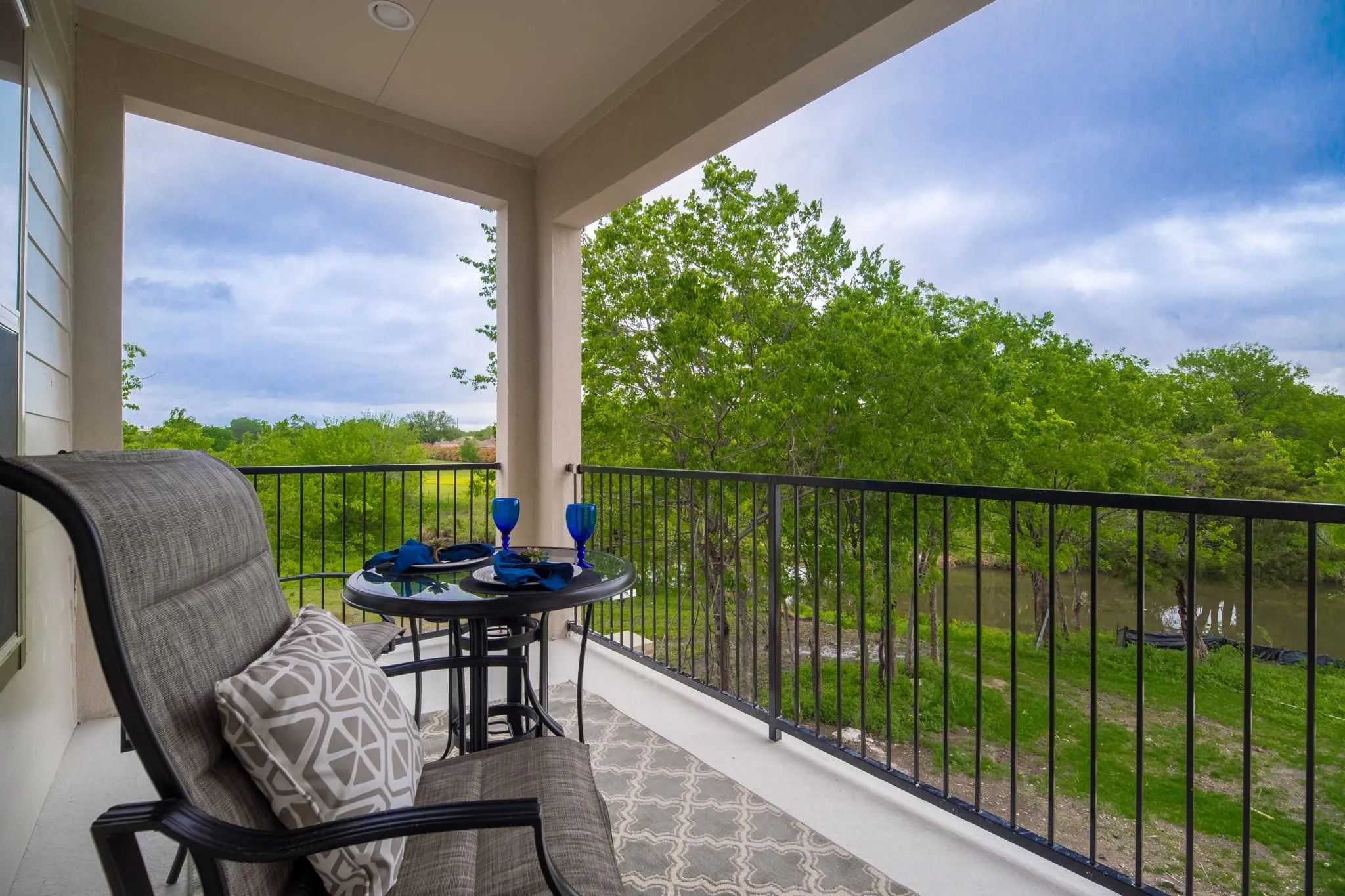 The property features a balcony with a black metal railing and views of lush green trees and a body of water