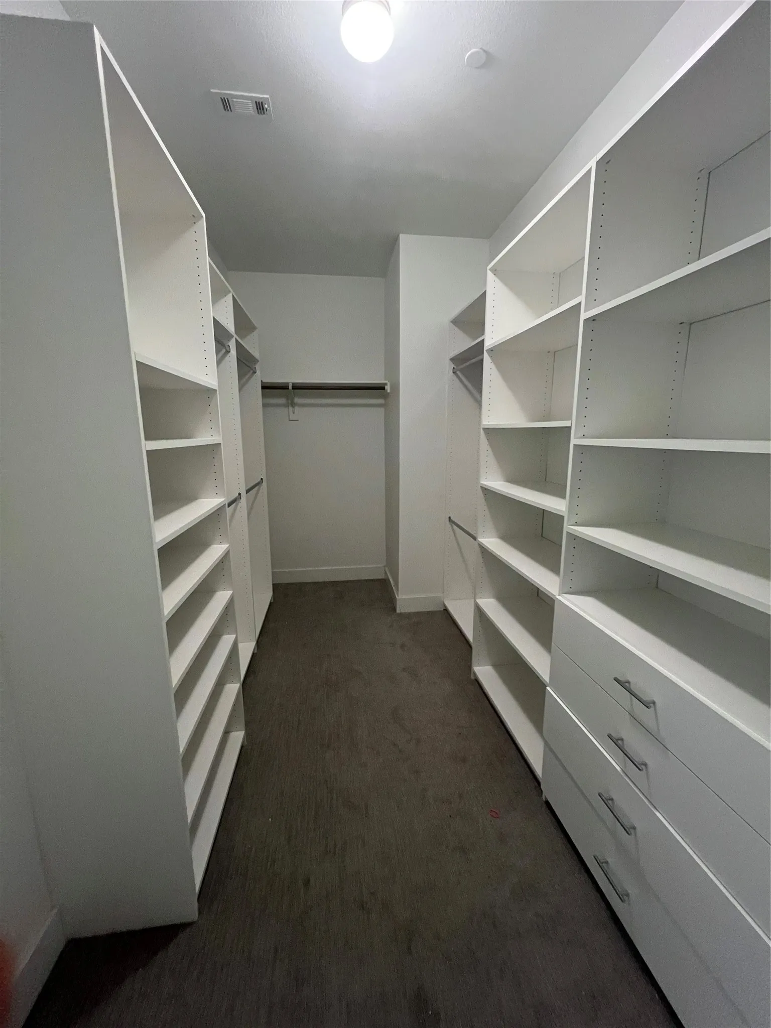 Custom walk-in closet featuring built-in white shelving, integrated drawers with brushed nickel hardware, and hanging rod storage