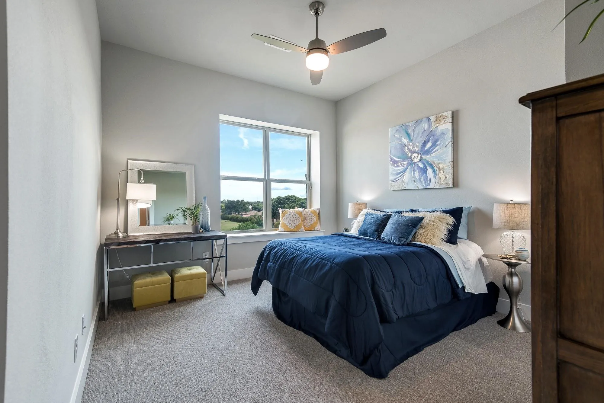 This room features a ceiling fan with integrated lighting, a large window providing views of the landscape, and carpeted flooring