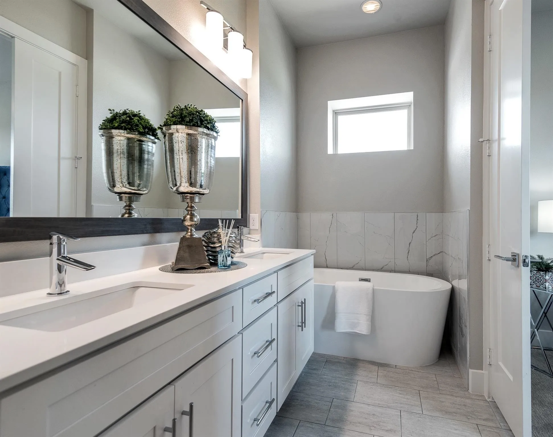 Well-appointed bathroom featuring a double vanity with ample storage, a large mirror, and a freestanding bathtub against a tiled wall